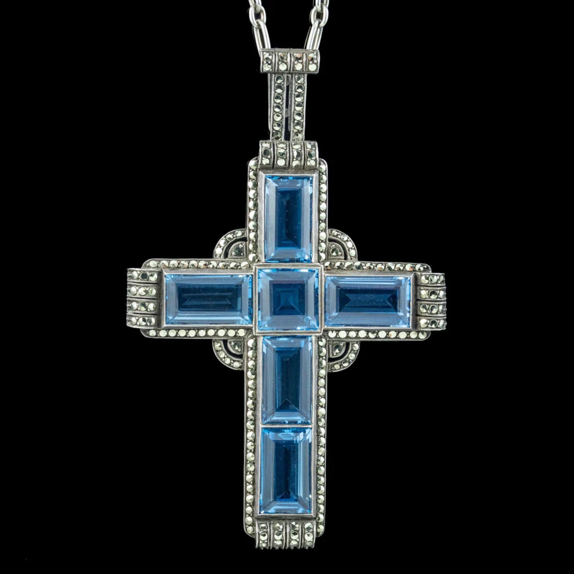 Un spectaculaire pendentif en forme de croix de style Art déco réalisé par le célèbre joaillier allemand Theodor Fahrner au début des années 1900. La croix est sertie de six magnifiques spinelles bleus synthétiques taillés en escalier, totalisant