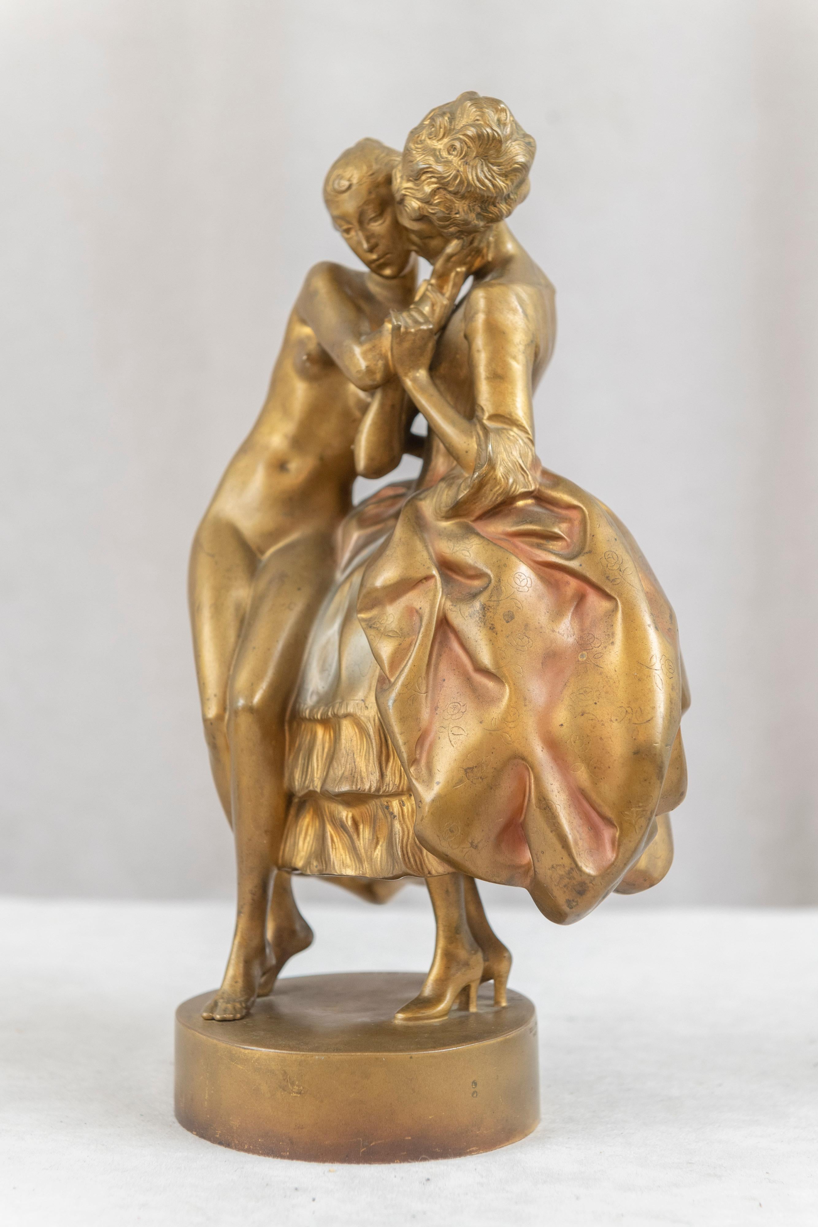  Ce magnifique bronze, chaleureux et affectueux, représente deux femmes qui s'embrassent. L'une est habillée de façon très formelle et pimpante, tandis que sa partenaire est nue. Le style et surtout les visages sont purement art déco. Le bronze a