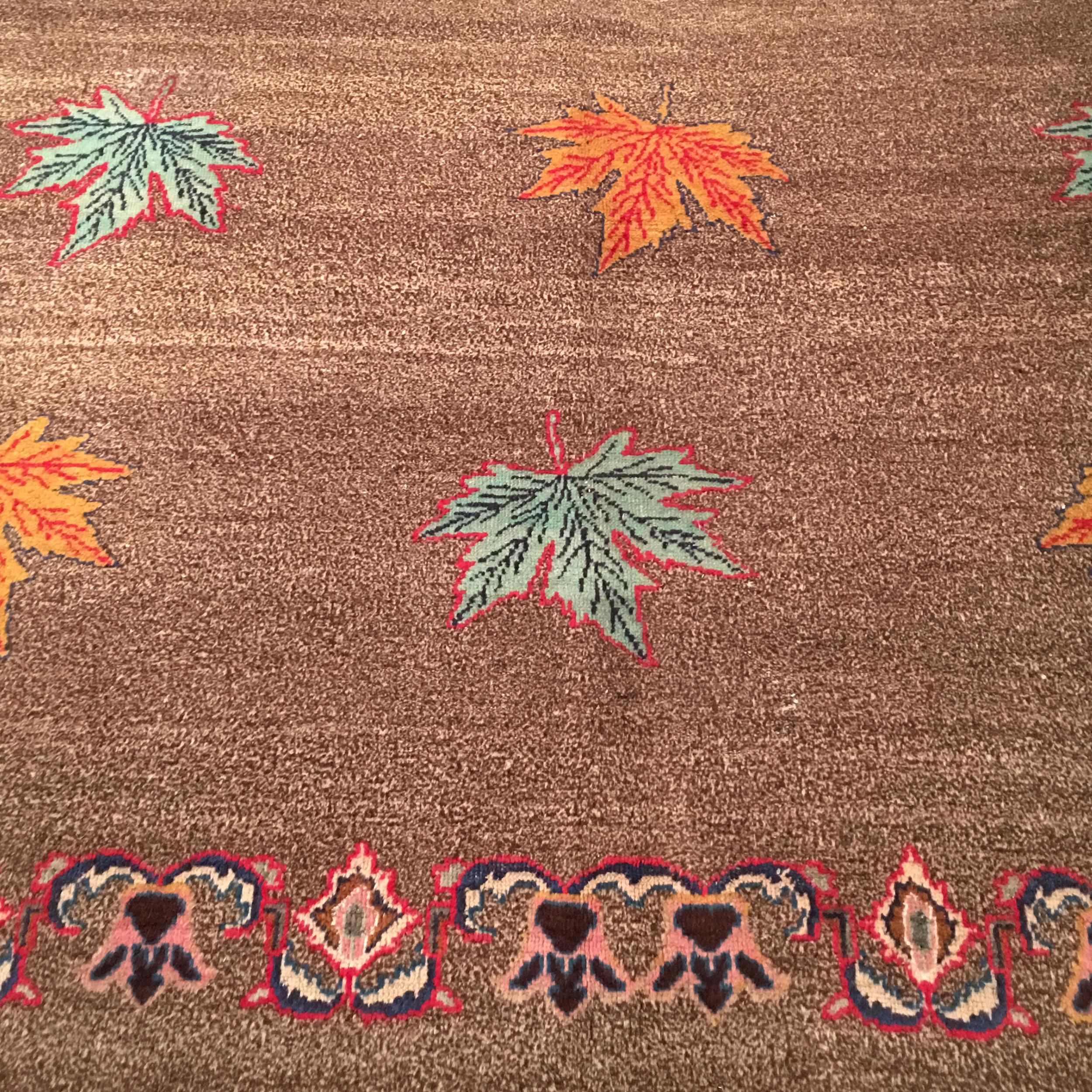Tapis indien Art Déco très inhabituel caractérisé par un motif sur toute la surface composé de grandes feuilles d'érable polychromes soigneusement placées sur un fond brun poivre et sel et ivoire, encadré par une bordure classique de type oriental.