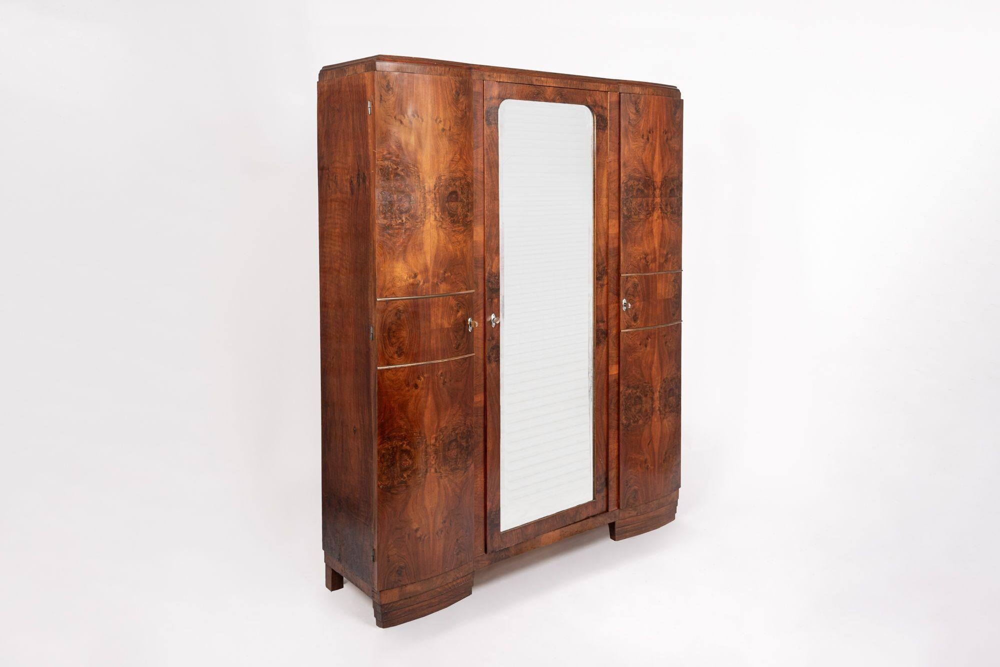 This antique Art Deco walnut wood armoire wardrobe cabinet with interior shelves is circa 1930. It is handcrafted from solid wood and burl wood veneer with beautiful matchbook grain patterning. The armoire features a full-length mirrored center door