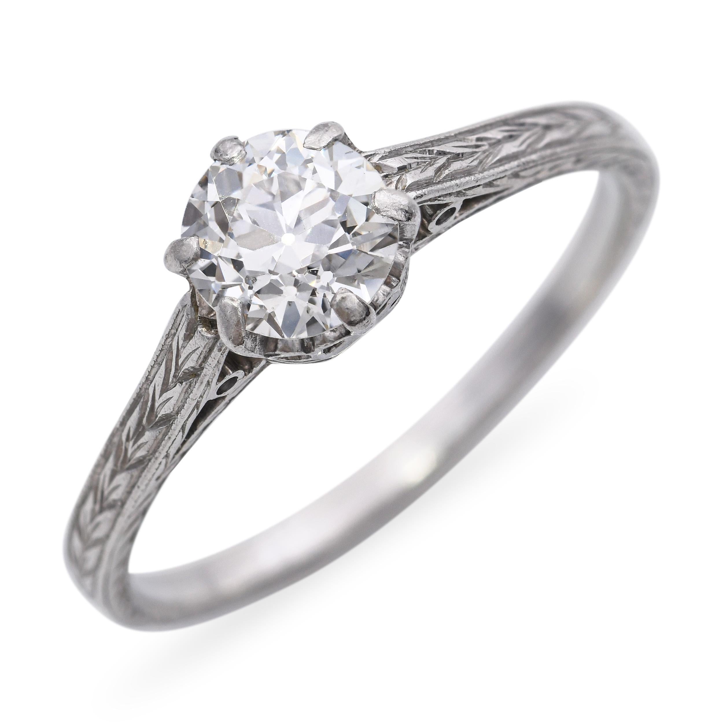 This exquisite Art Deco engagement ring is crafted in platinum and features a bright 0.73ct Old European cut diamond set in a refined six-prong setting. The shoulders are delicately hand-carved with intricate patterns, a hallmark of the era’s