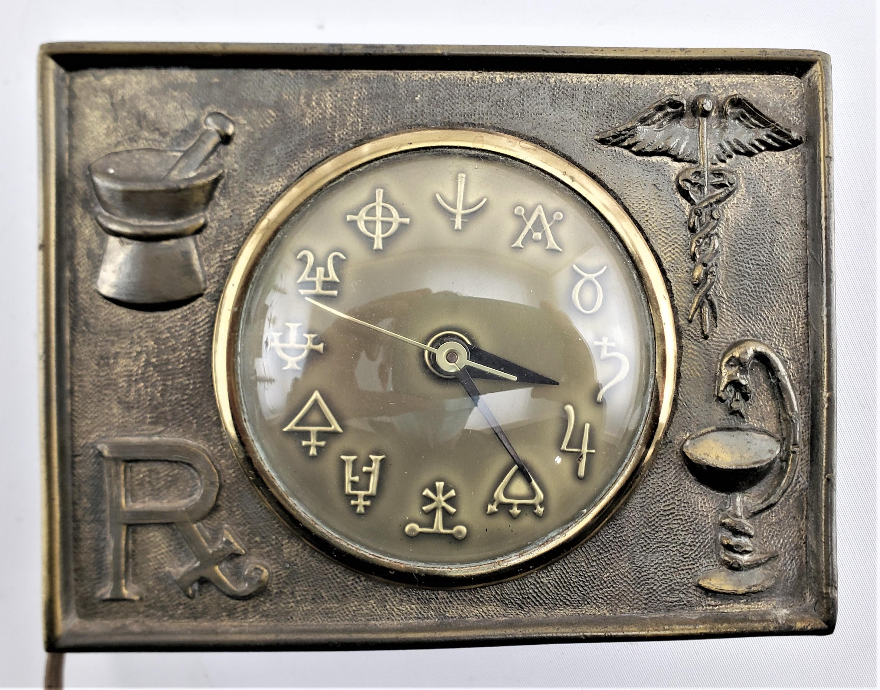 This antique desk or table clock has no maker's marks, but is presumed to have been made in the United States in approximately 1920 in the period Art Deco style. The cock face is done in a patinated cast brass and has iconic pharmaceutical or