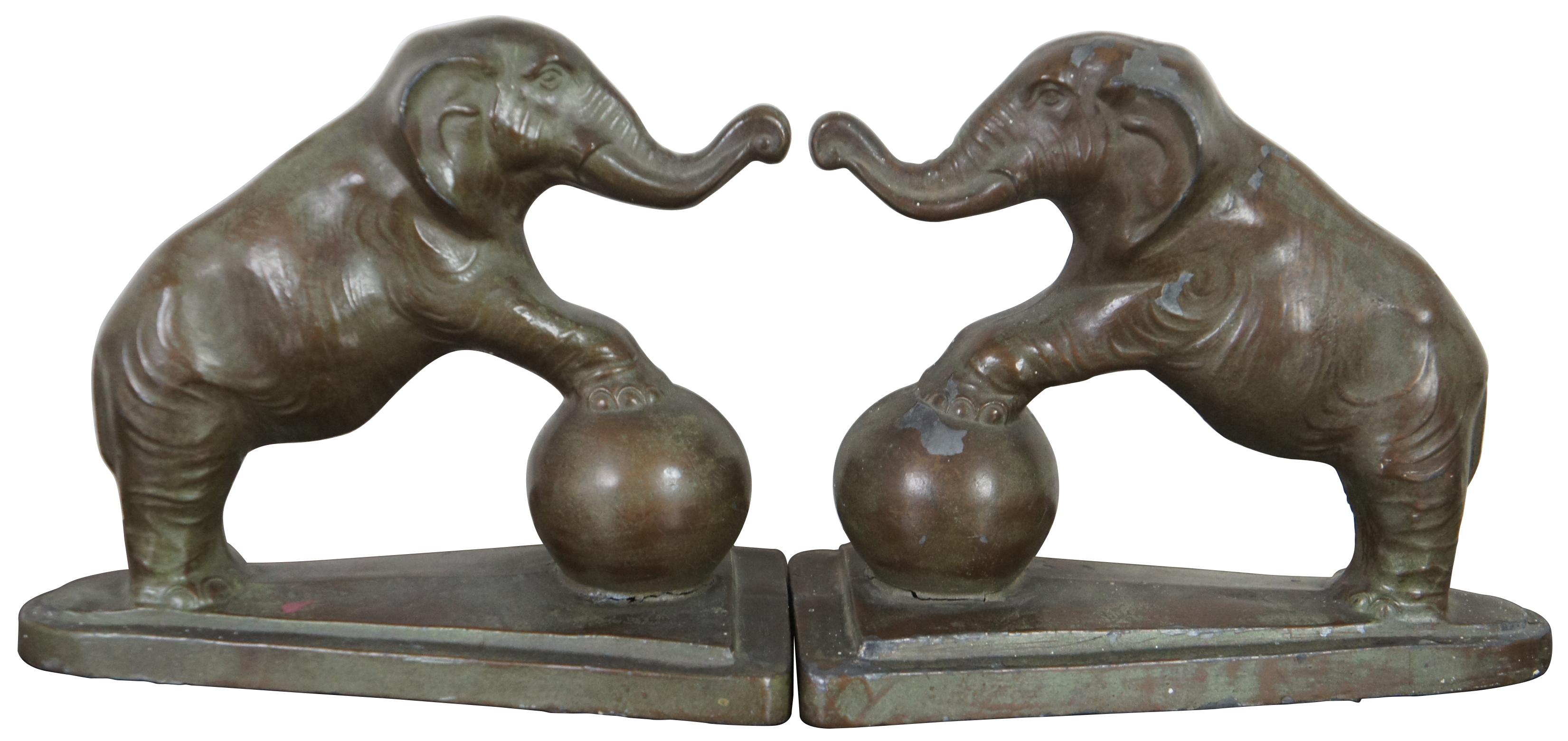 Antique Art Deco metal bookends in the shape of elephants with raised trunks, front feet balanced on a large ball and triangular base.
 
