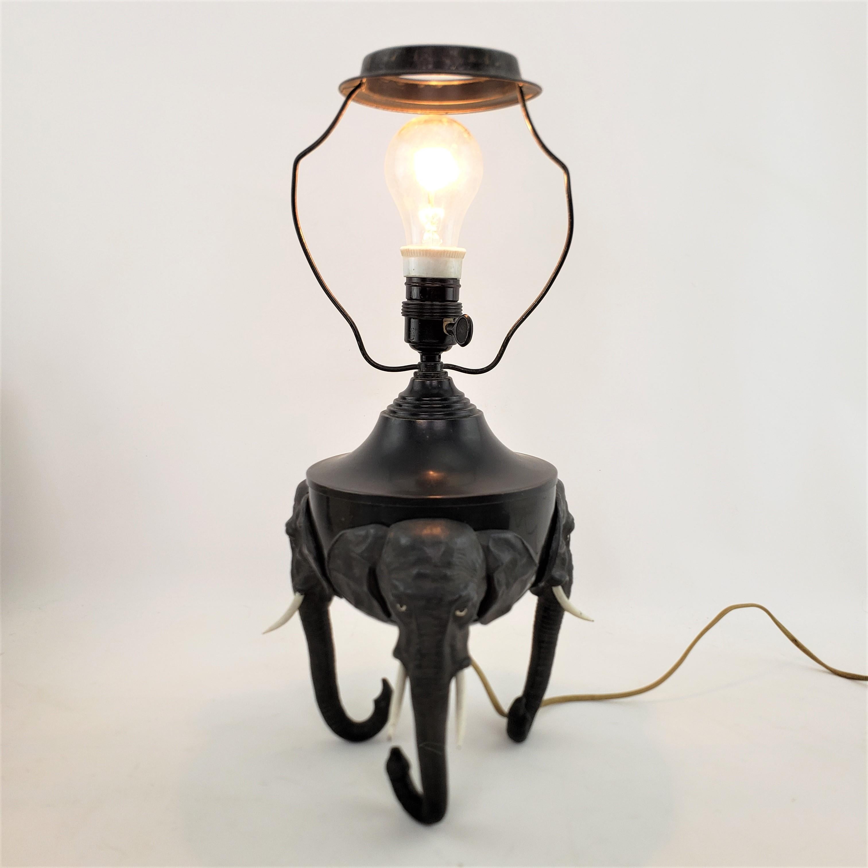 This unique metal table lamp is unsigned, but presumed to have originated from France and dating to approximately 1920 and done in the period Art Deco style. The lamp is composed of a metal body with three cast spelter elephant heads on the sides,