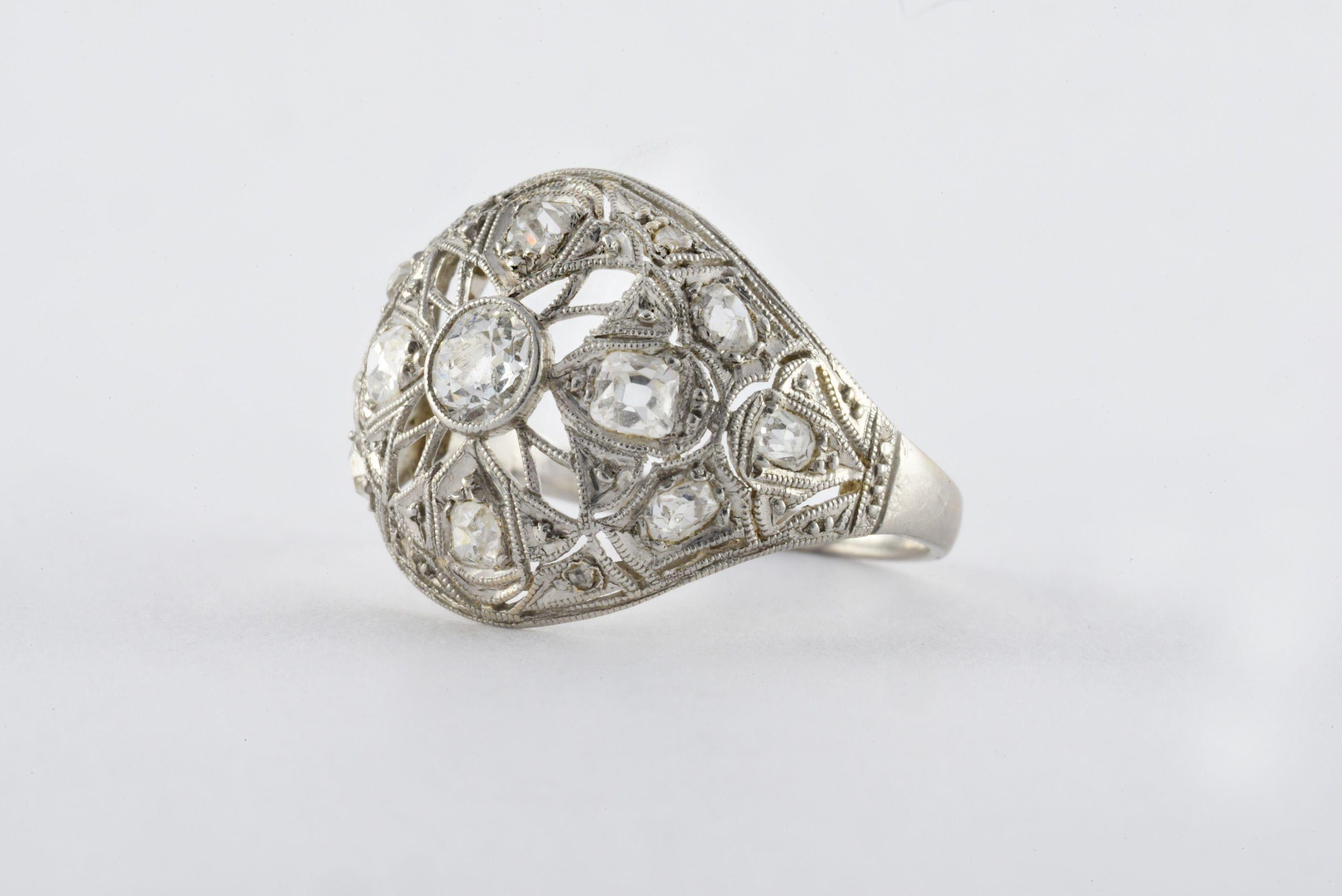 Crafted from platinum, this early Art Deco era ring sparkles in an openwork design with four Old Mine cut diamonds surrounding a larger Old European cut diamond center stone measuring approximately 0.30 carats. The decoratively pierced dome is