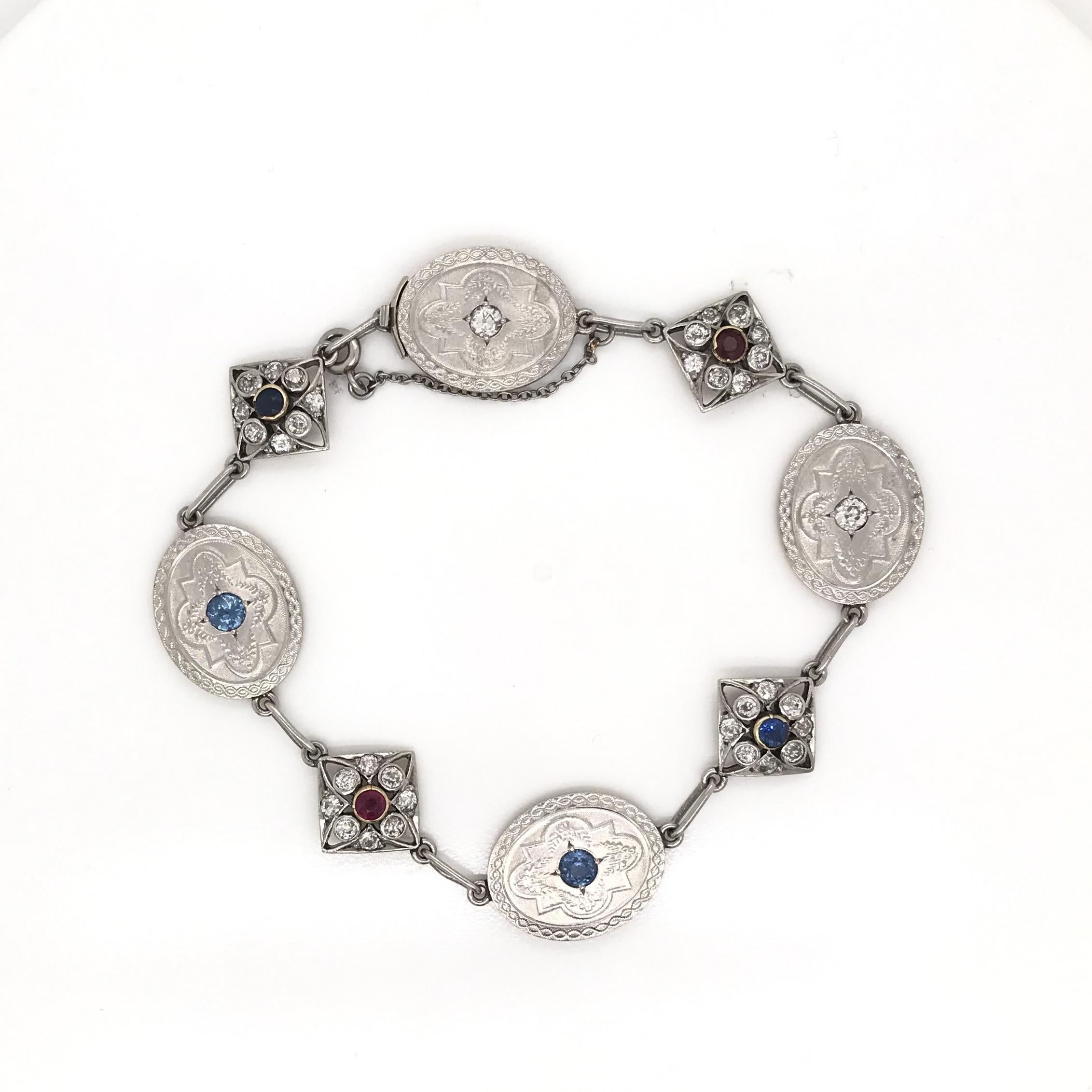 This antique piece was crafted sometime during the Art Deco design period (1920-1940). The bracelet features alternating filigree charm and medallion links. Each platinum medallion features extensive engravings along with sapphire and diamond