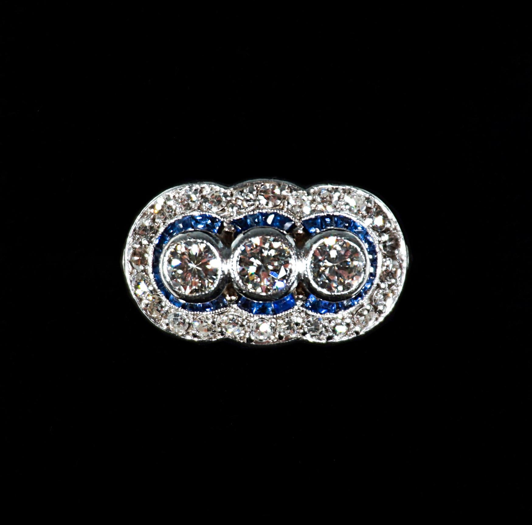 Delicate antique baguette-shaped old brilliant-cut diamond ring, with three old cut diamonds centered in a row estimated 1.10 carat altogether, surounded by small sapphires and in a millegrain openwork collet, framed with numerous octagonal