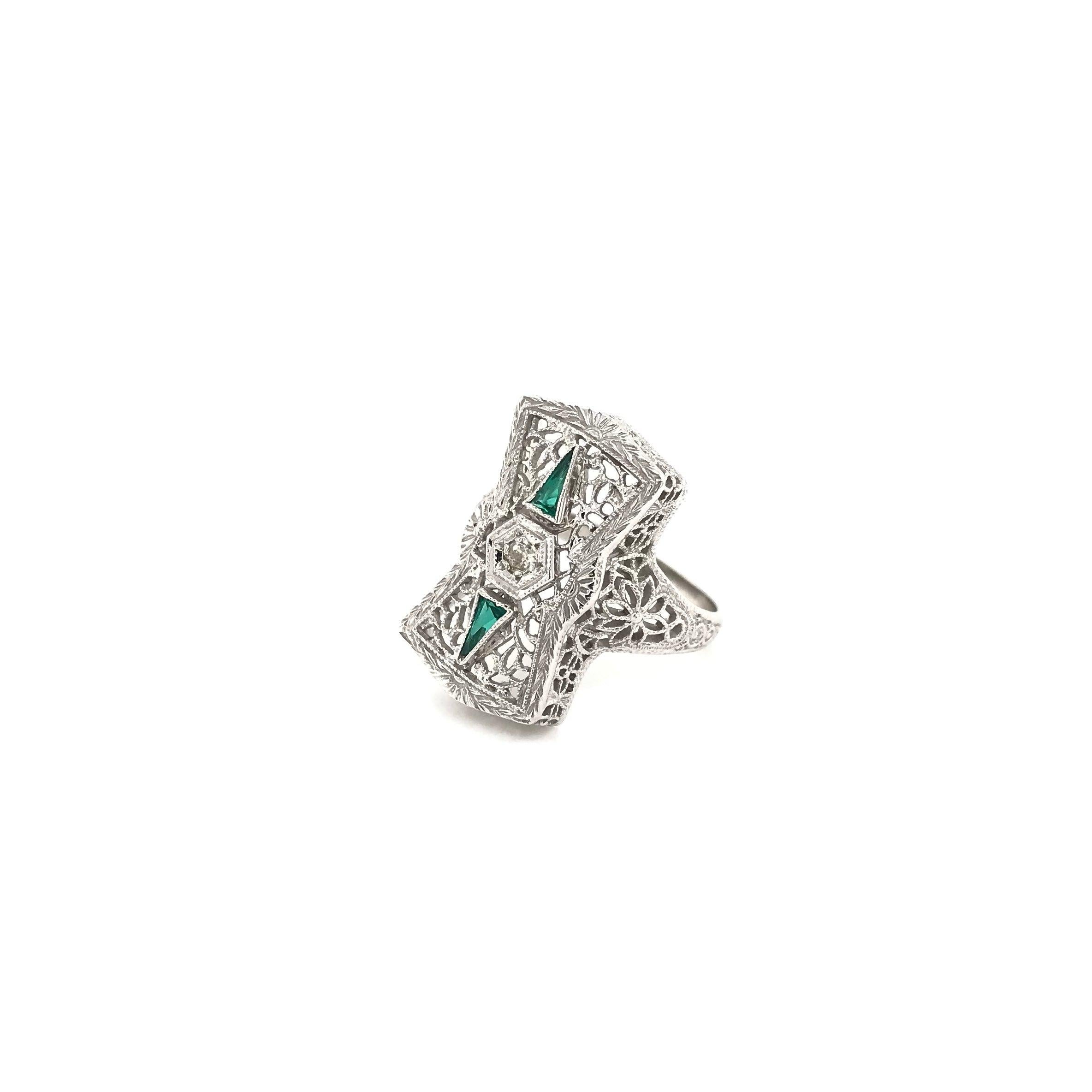 This exceptional antique piece was handcrafted sometime during the Art Deco design period (1920-1940). The 14K white gold setting features extensive exceptionally fine floral filigree, custom cut emerald accents, incredible milgrain work, and one