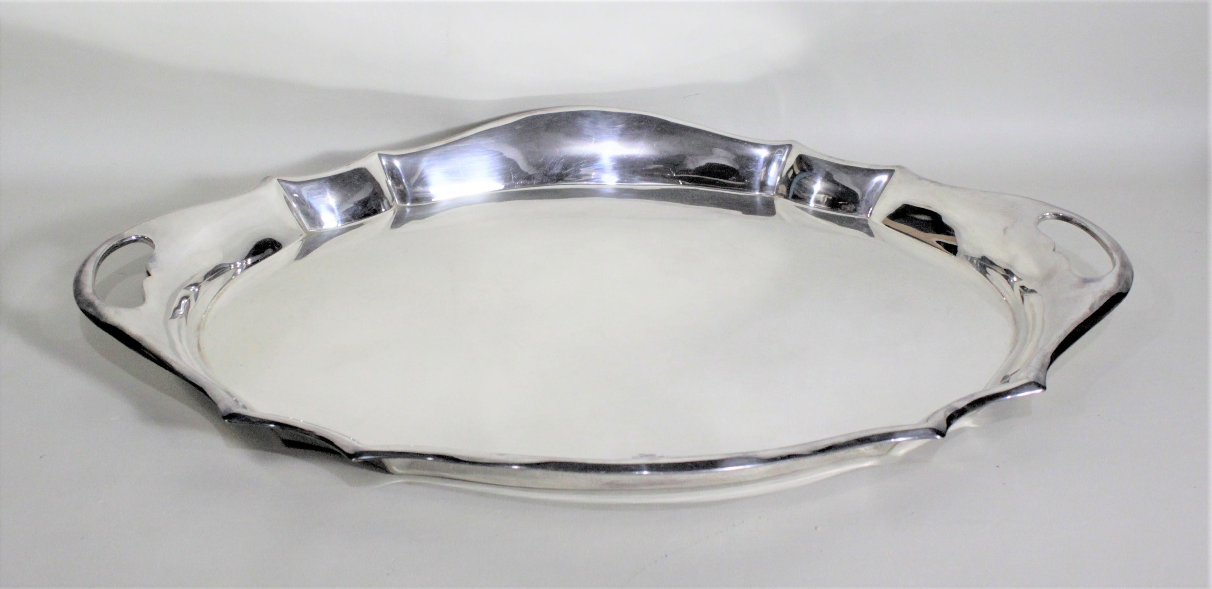 This antique silver plated serving tray was made in England in circa 1920 in a very modern streamlined design in the Art Deco style. This oval shaped tray has solid raised sides with a simple scrolling curved edges and handles cut in on either end.