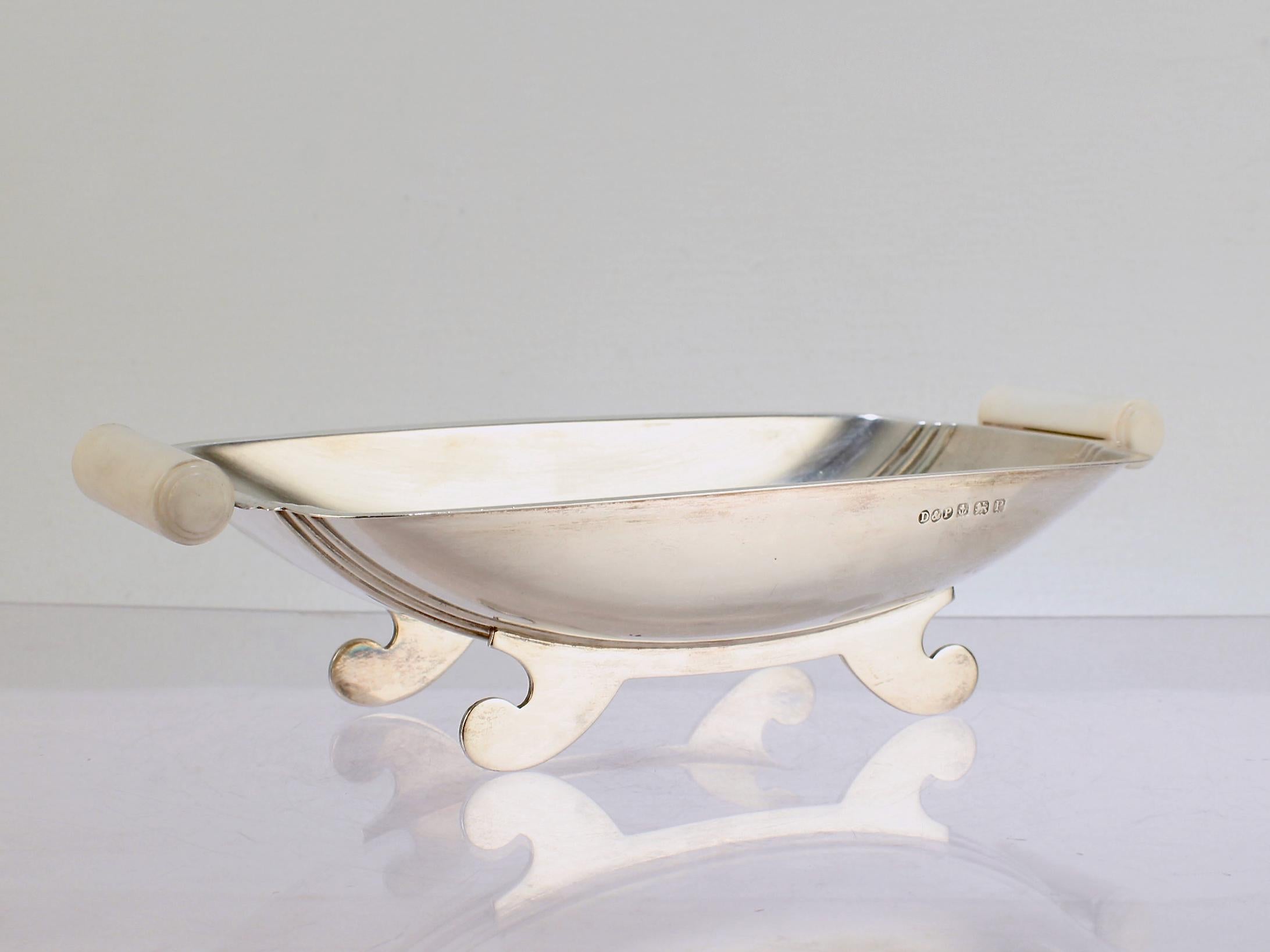 A fine Art Deco bowl in sterling silver.

By Davies & Powers of Birmingham, England. 

The bowl has curved feet and cleats supporting a shaped bowl that is mounted with 2 early white early plastic handles. These handles are likely a material