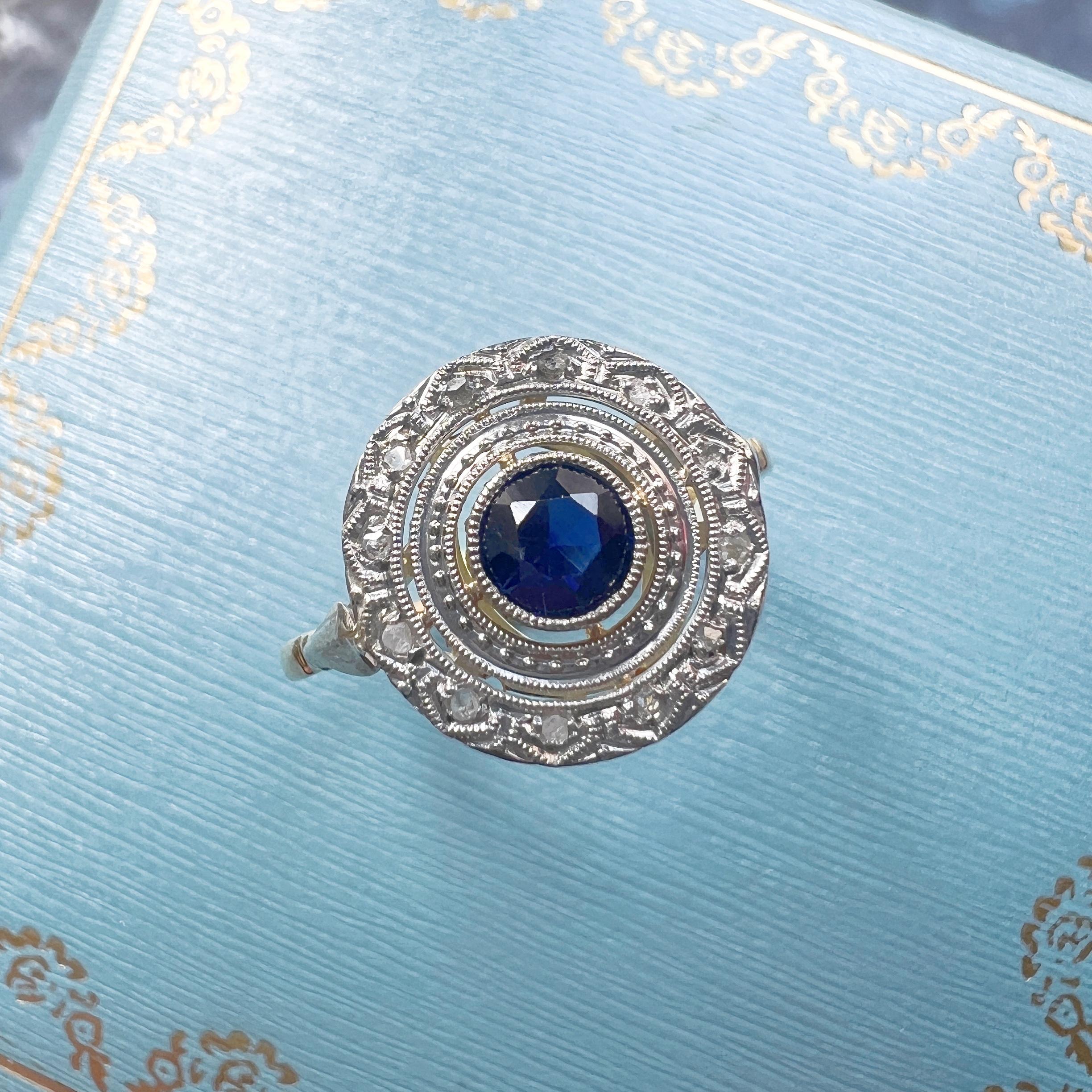 For sale an antique ring, crafted during the late 19th to early 20th century. This captivating piece showcases a stunning blue sapphire, encircled by a halo of rose cut diamonds, creating a mesmerizing cluster design.

At the center of this