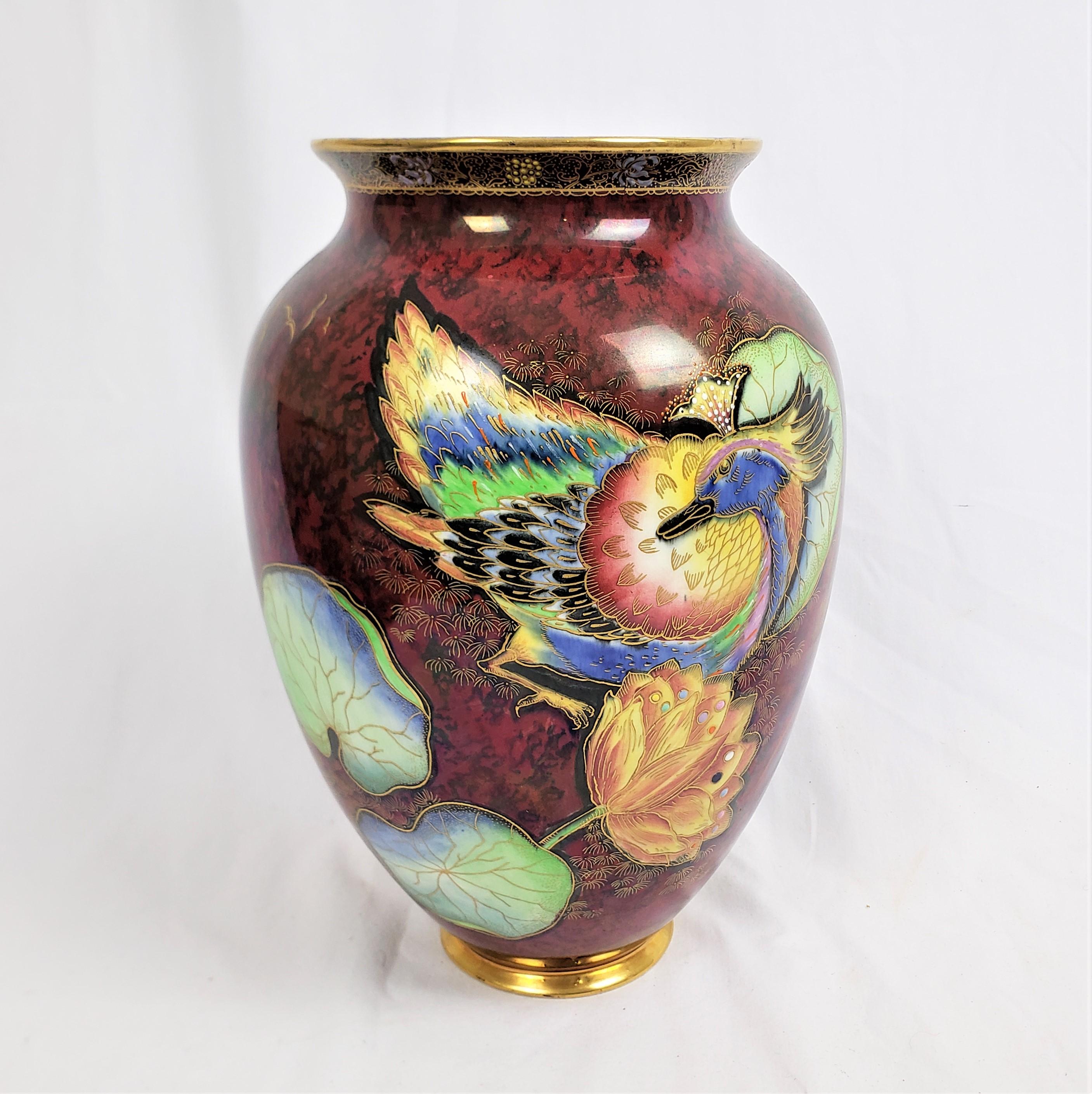 This antique vase was made by the renowned Carlton Ware factory of England in approximately 1920 and done in the period Asian inspired style. The vase is done in pottery with a mottled black and burgundy ground with vibrantly colored exotic birds