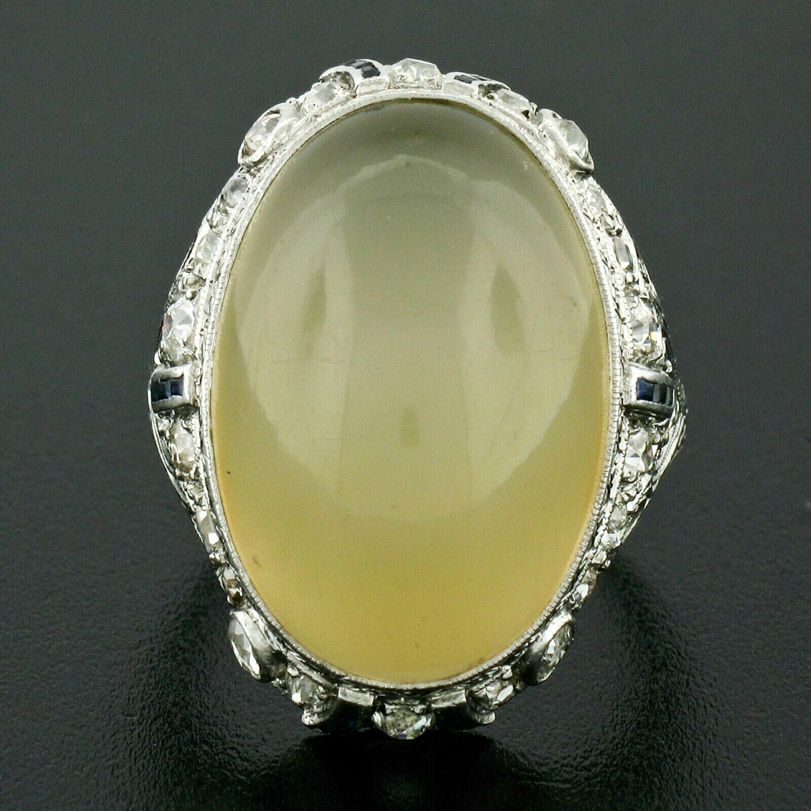 This magnificent antique cocktail ring was crafted from solid 900 platinum during the art deco period. The ring features a large, approximately 22x15mm, translucent pale yellow moonstone bezel set at its center. The center stone is surrounded by