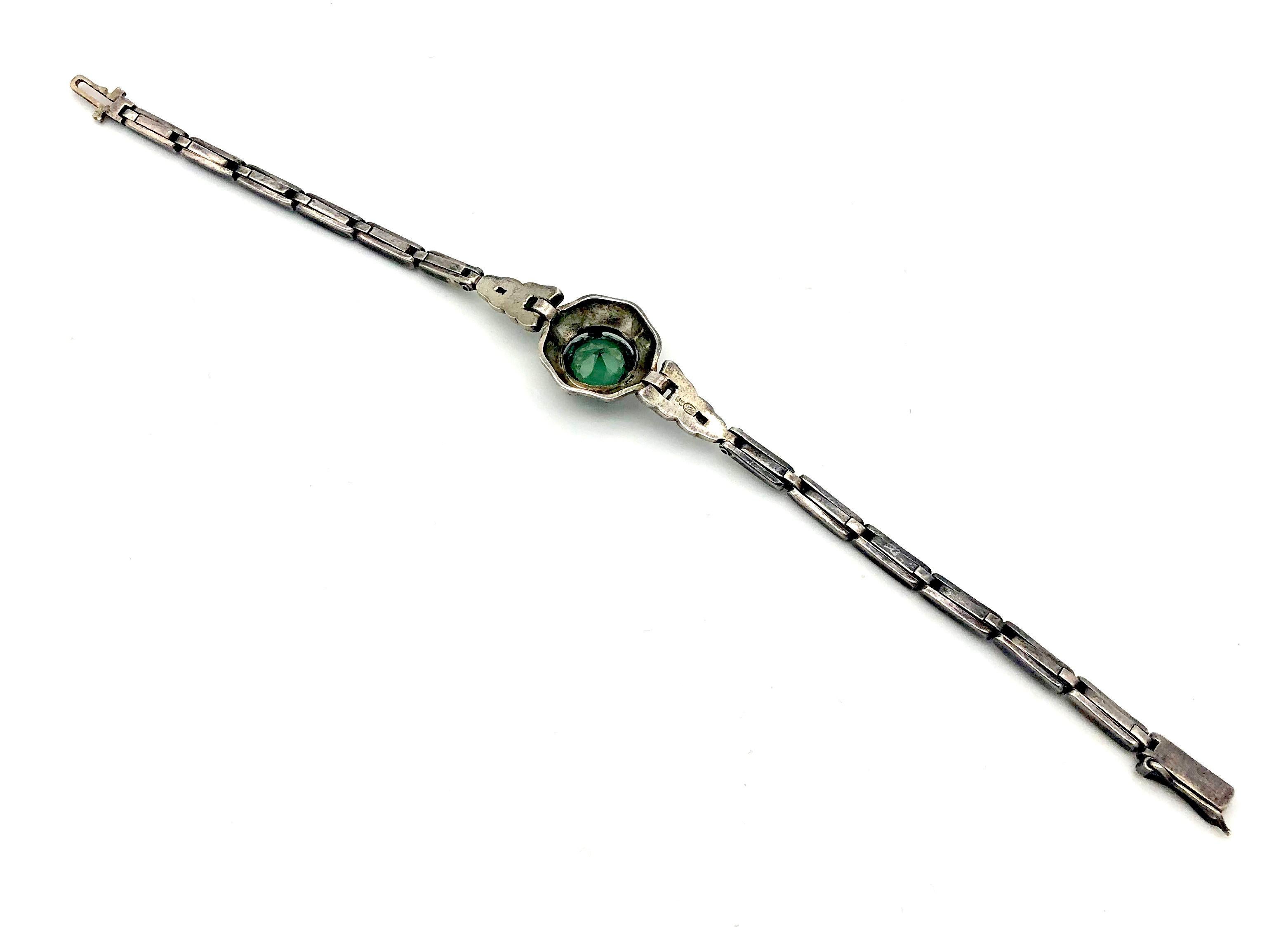 This elegant silver Art Deco link bracelet was made in 1920 ca. The octagonal centerpiece with softened edges is set with a deep gras green glass stone. To either side the center piece is embedded by typical Art Deco elements, one of which is