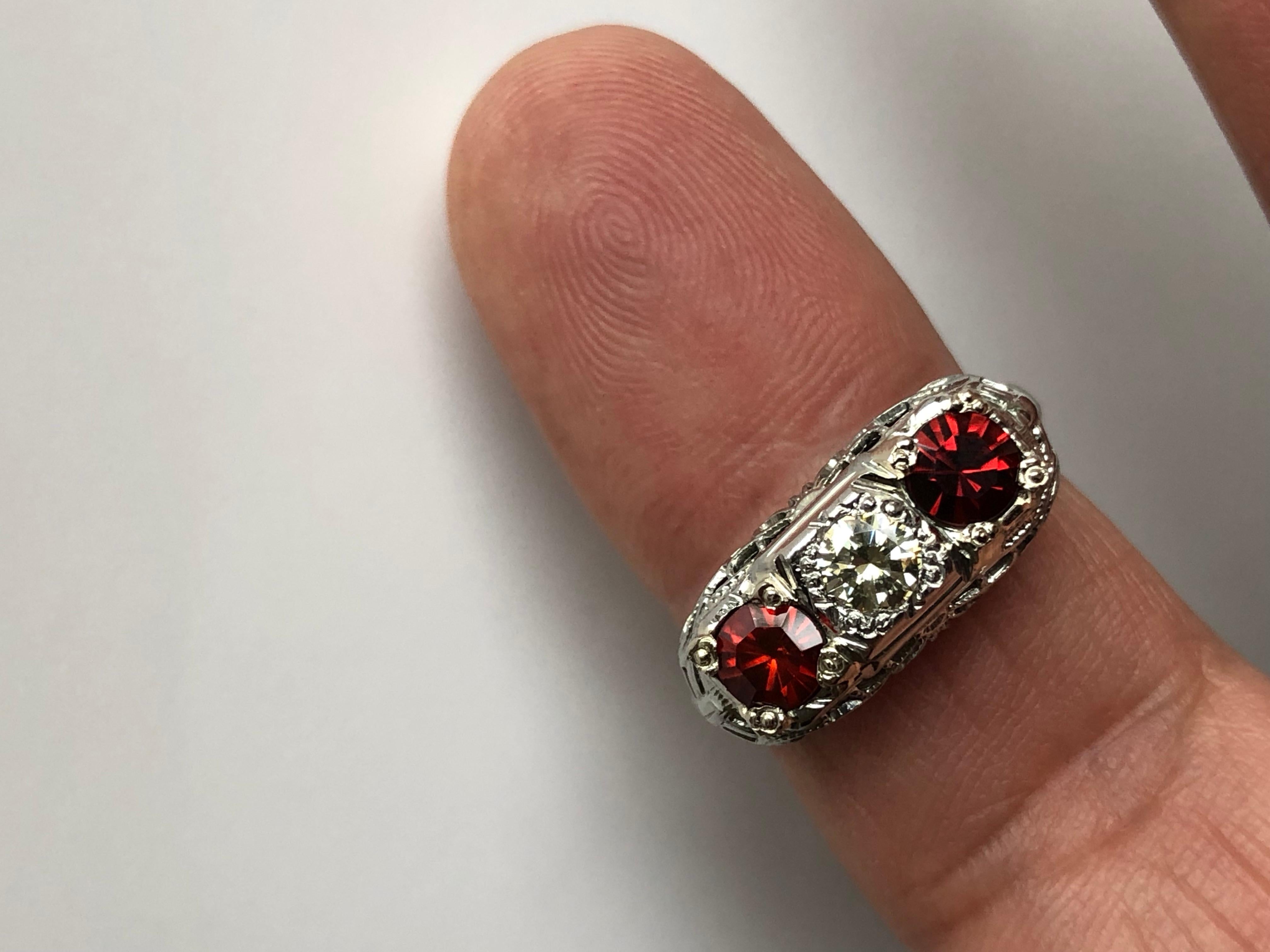 1940 raised top filigree Art Deco Style ring centering a sparkly round cut diamond weighing approx. 0.30 carat color N, VS. And on each side a gorgeous red-orange spinel round cut VS approx. .90 carats total weigh.
Total Gemstone weight: Approx.
