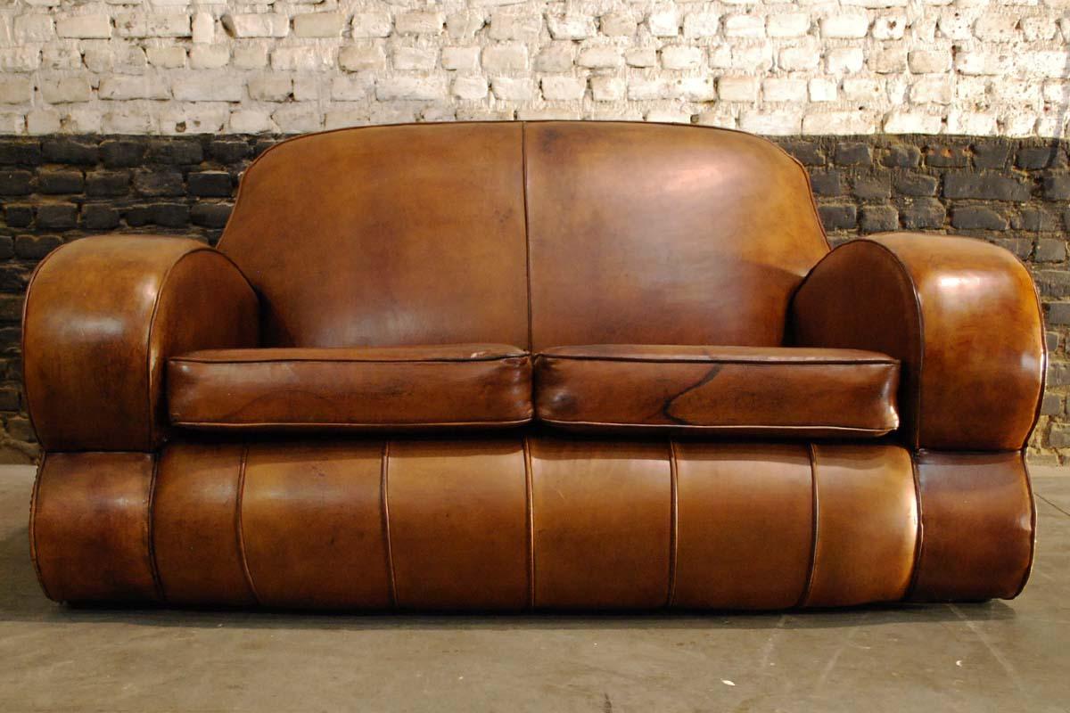 This beautiful two-seat sofa is upholstered in its original hand patinated sheep leather. It was made in France and dates approximately 1915. It’s shape and construction make it a typical Art Deco club sofa. The sofa has been upholstered with the