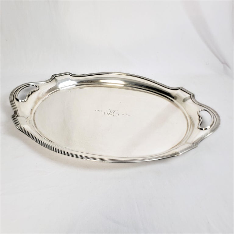 This antique presentation oval serving tray was made by the Gorham Company of the United States in approximately 1920 and done in the period Art Deco style. This heavy and substantial tray is composed of sterling silver with stepped raised sides