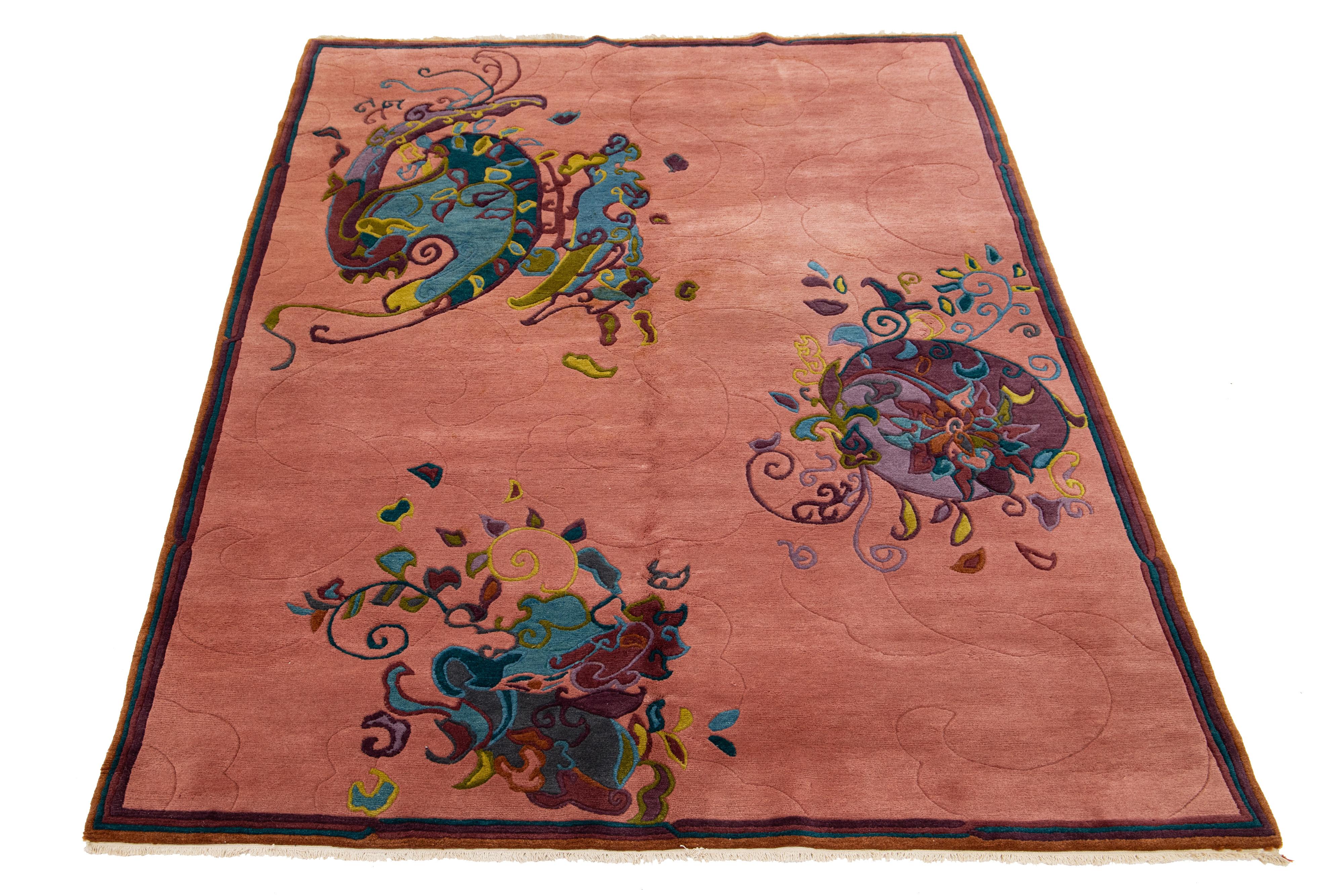 Questo squisito tappeto antico cinese Art Deco è annodato a mano con lana di alta qualità. Presenta un delizioso sfondo color salmone chiaro ornato da un vivace disegno floreale multicolore, elegantemente bordato di viola, blu e marrone.
Questo