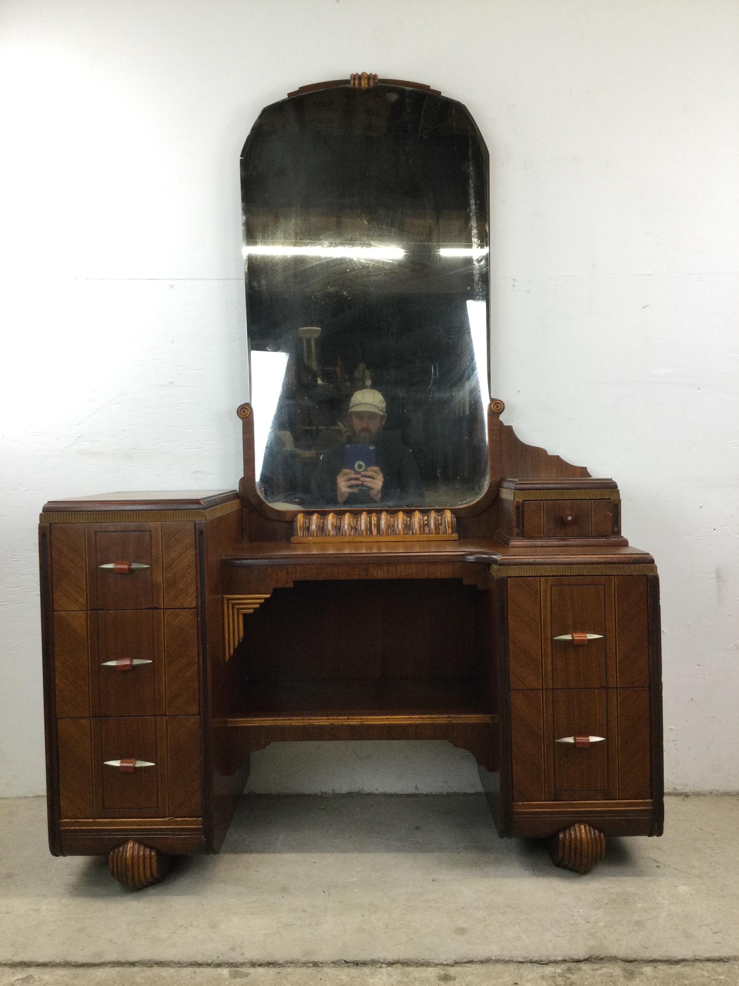 This antique Art Deco mirrored vanity features hardwood construction, beautiful walnut veneer with original finish, six dovetailed drawers with chrome & bakelite drawer pulls, attached antique mirror, and unique carved wood feet. Included is a