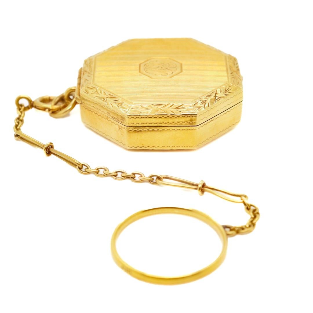 A fine Art Deco ladies' finger ring compact.

In 14k gold.

Of an octagonal shape with a hinged lid, fitted mirror, and attached finger ring & chain.

With engraved & engine-turned decoration throughout and a monogrammed cartouche to the lid.

These