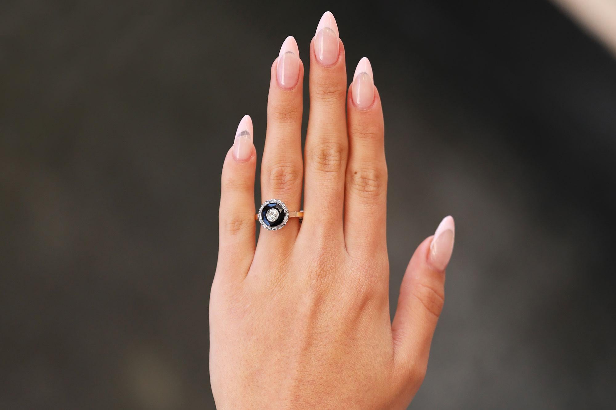 A unique and striking antique Art Deco engagement ring centered by an old mine cut diamond floating in a black onyx pool. This antique target ring displays both rich 18k yellow gold and cool platinum for a two tone vibe. The chunky main diamond set