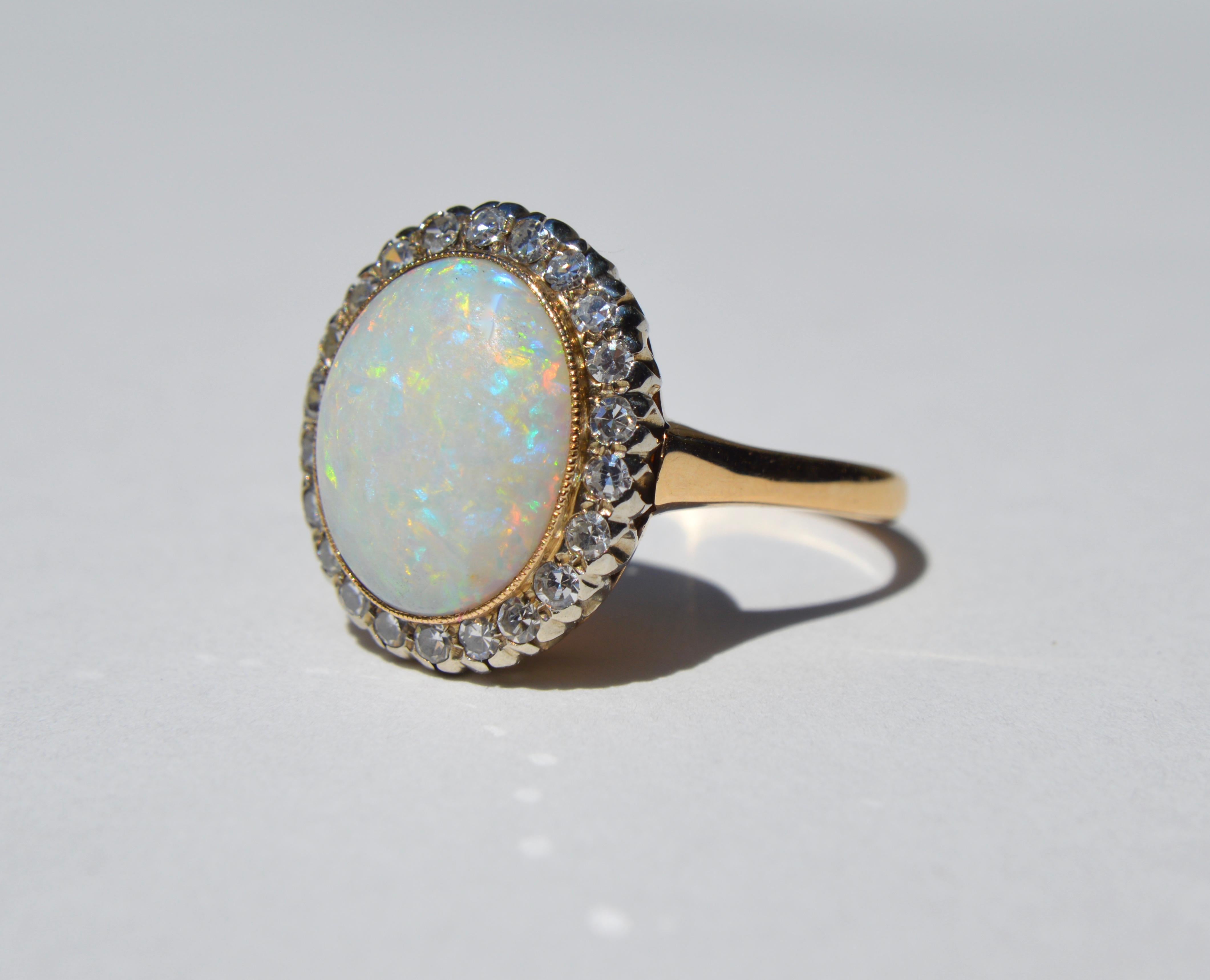 Beautiful Art Deco era circa 1920s fiery Australian opal with old European cut diamond halo. 14K yellow gold. Size 10. Can be resized by a jeweler. Opal cabochon measures 14x10mm, 6 carats. Stamped as solid 14K. In very good condition. The opal is