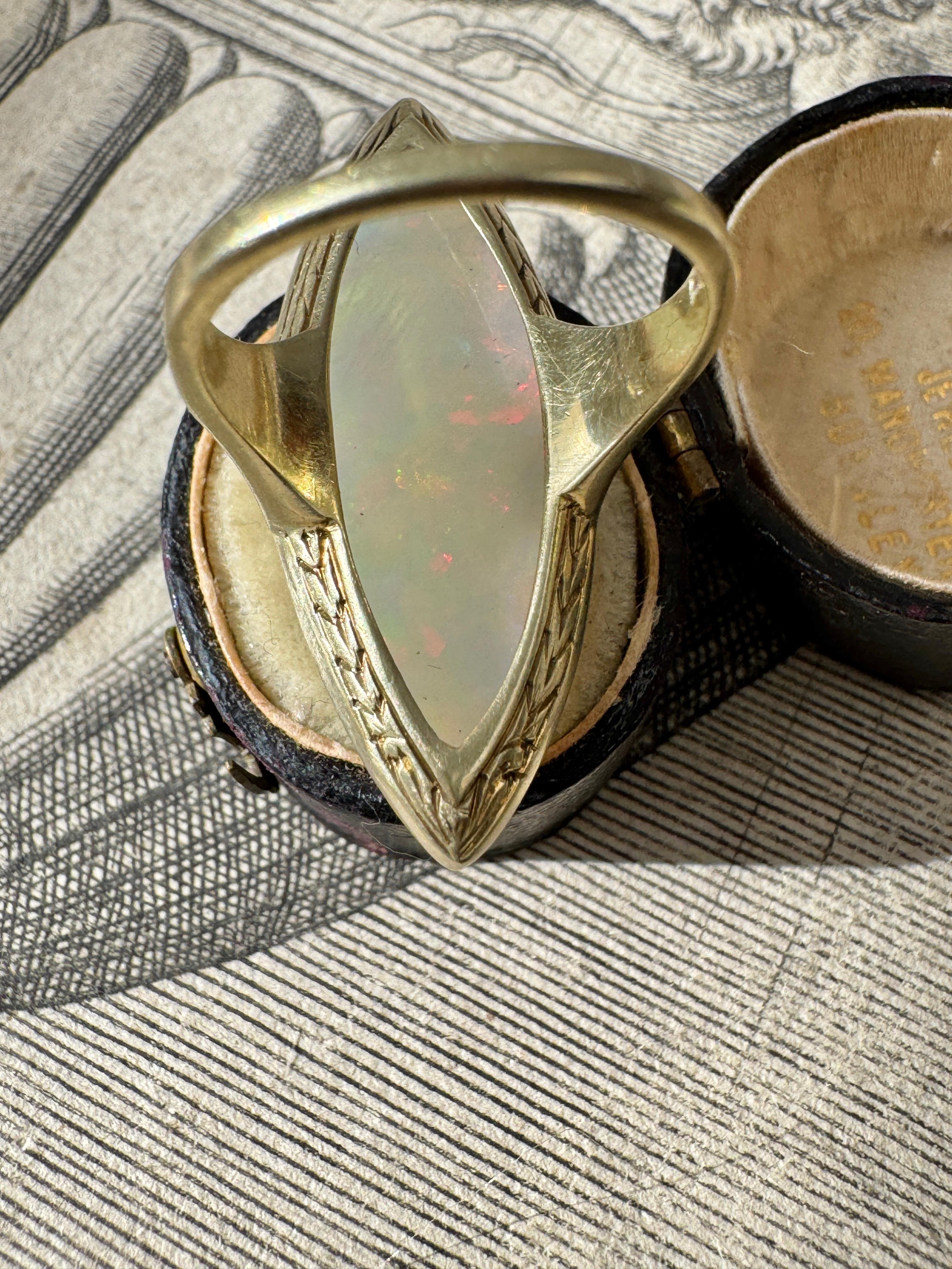 Sophisticated and streamlined, this elegant Art Deco ring showcases a 12.8 carat navette-shaped cabochon opal. The opal has a white body color with subtle flashes of color, creating a delicate play-of-color effect. Crafted in 14 karat yellow gold,