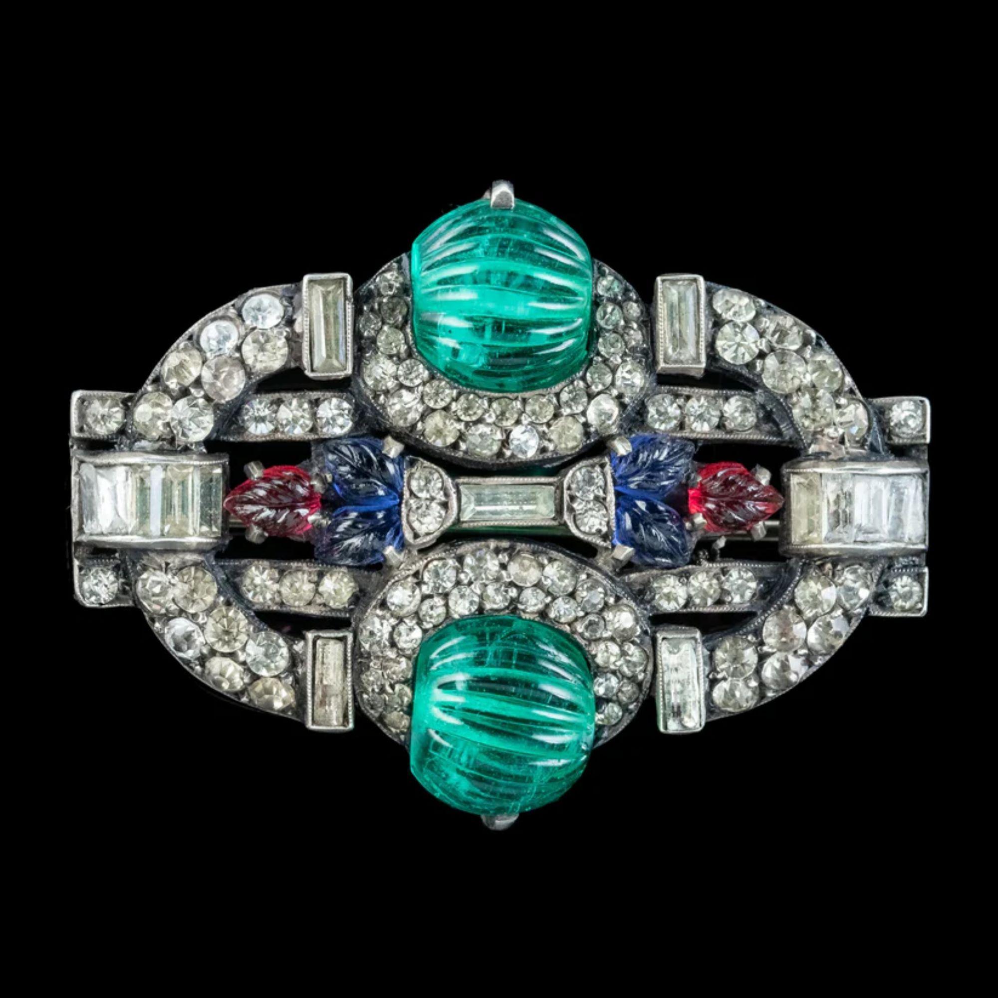 A glitzy antique Art Deco brooch from the 1920s decorated with glistening, clear pastes, a contrasting combination of round and baguette cut. Two ribbed green tourmaline spheres top and tail the gallery with blue and red paste leaves along the