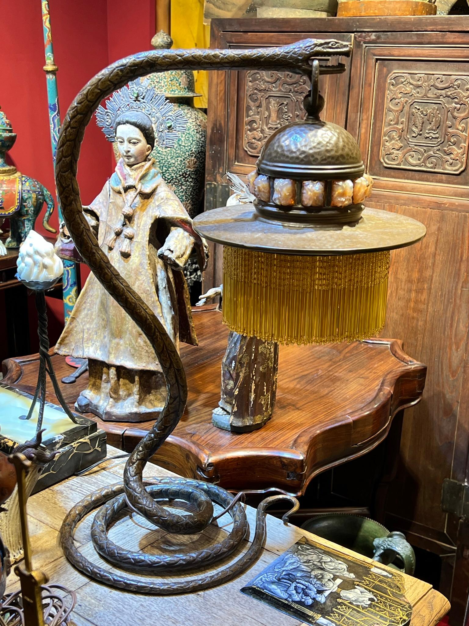 Notre lampe de table en bronze patiné d'époque Art déco, à la manière d'Edgar Brandt, est façonnée en forme de serpent enroulé avec un abat-jour en métal martelé suspendu à sa bouche. L'abat-jour est décoré d'inserts en verre et de fines perles de