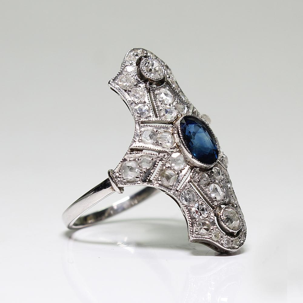 Period: Art Deco (1920-1935)
Composition: Platinum

Stones:
•	1 natural oval cut sapphire that weighs 1ctw.
•	2 Old mine cut diamonds of H-SI1 quality that weigh 0.40ctw. 
•	18 Rose cut diamonds of J-SI1 quality that weigh 0.60ctw.
•	22 Single cut