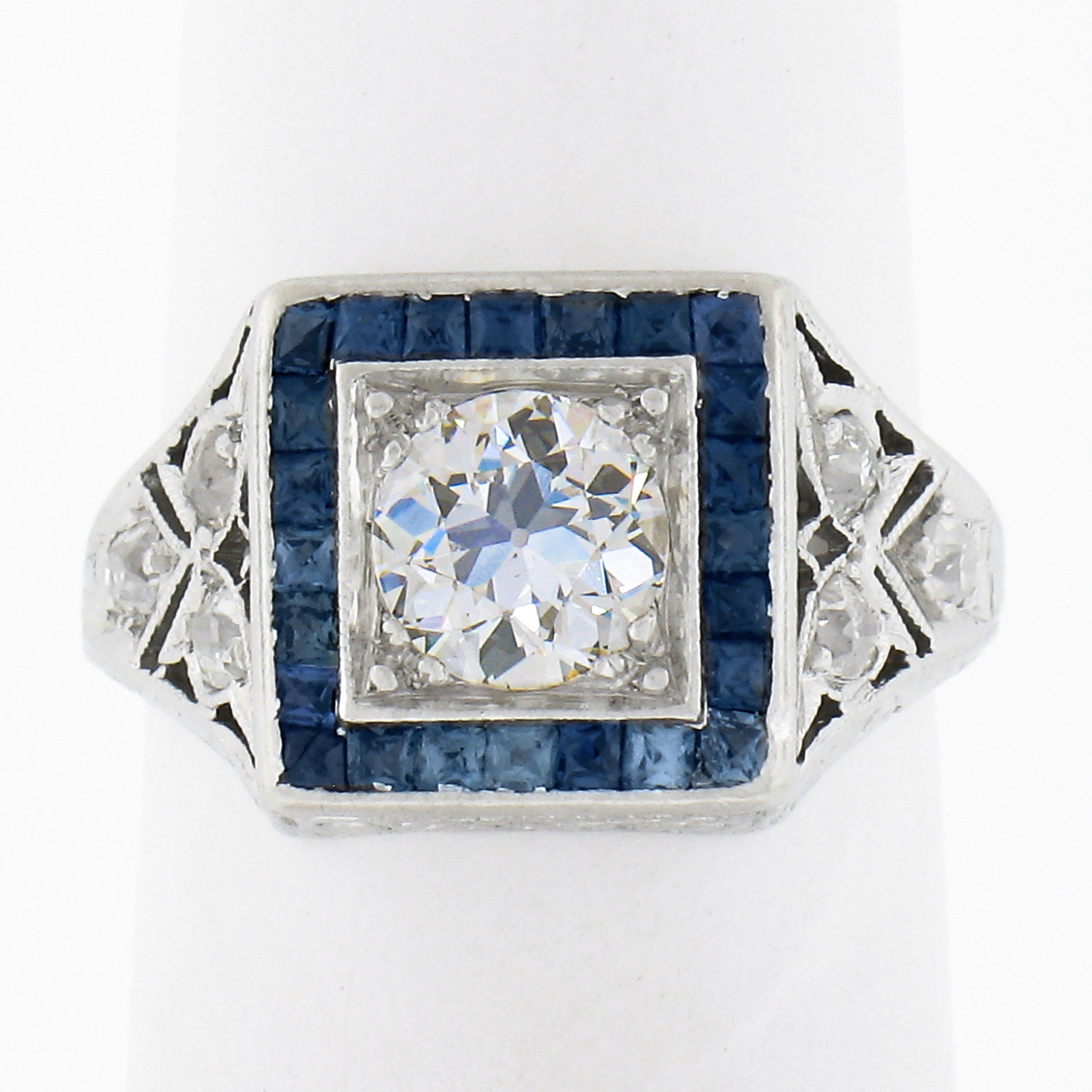 This gorgeous and very well kept antique engagement ring was crafted in solid platinum during the art deco period and features a stunning, approximately 0.52 carat old European cut diamond neatly prong set at the center of the squared sapphire halo