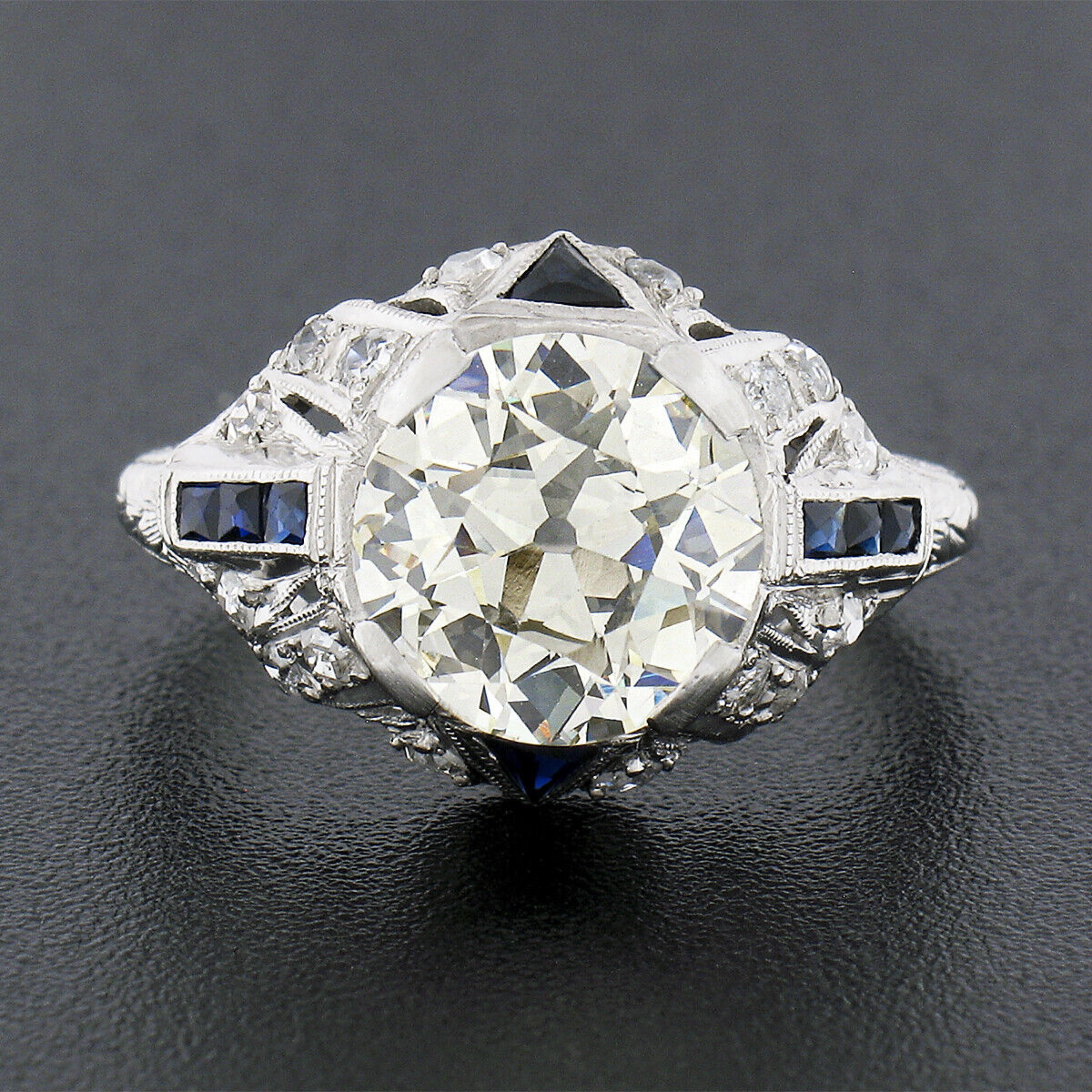 This absolutely breathtaking antique diamond and sapphire engagement ring was crafted from solid platinum during the art deco period and features a GIA certified old European diamond solitaire neatly prong set at its center. This incredible and