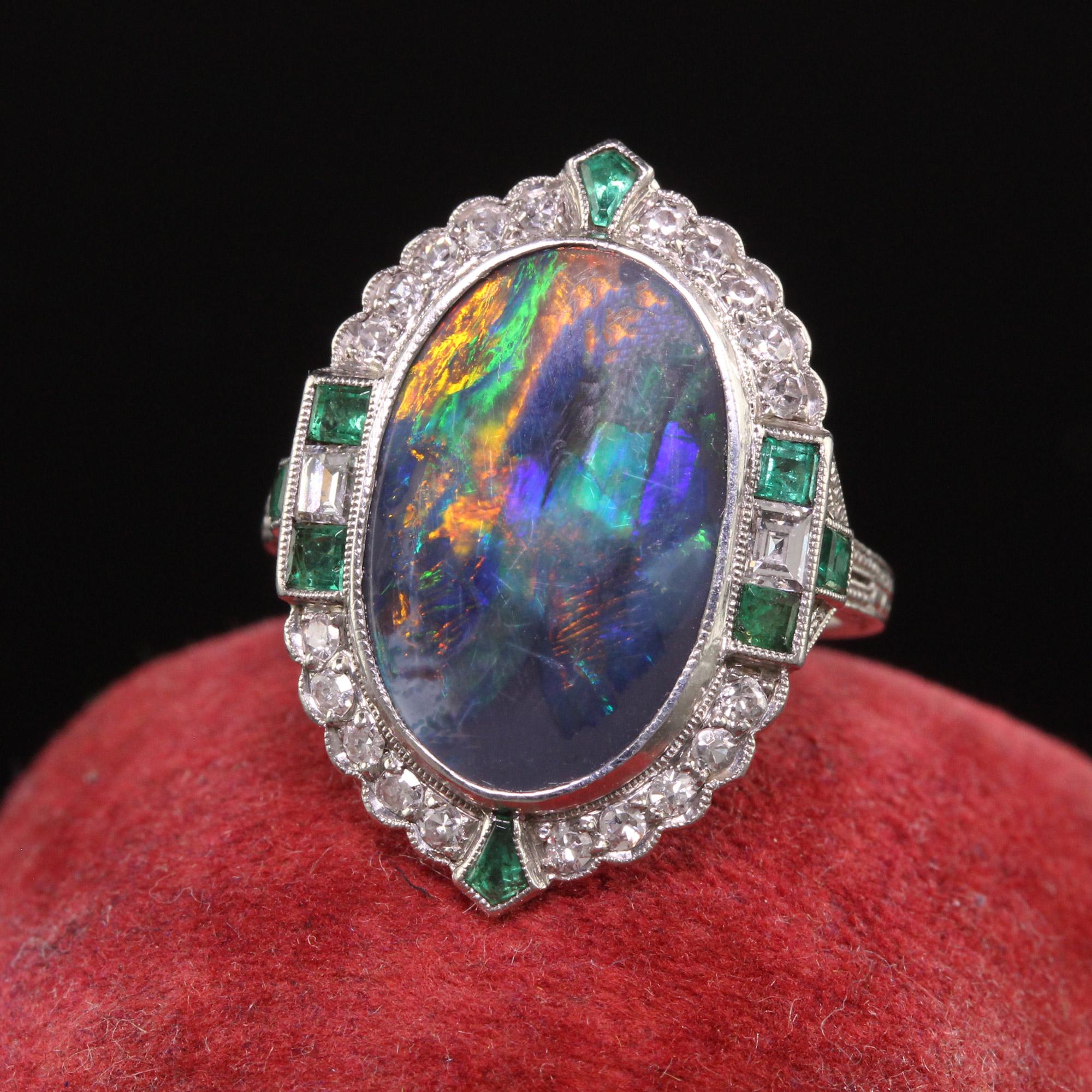 Beautiful Antique Art Deco Platinum Black Opal Diamond and Emerald Cocktail Ring. This gorgeous ring is crafted in platinum. The center holds an unbelievable black opal with a full play of color between red, blue, green, and orange. There are also