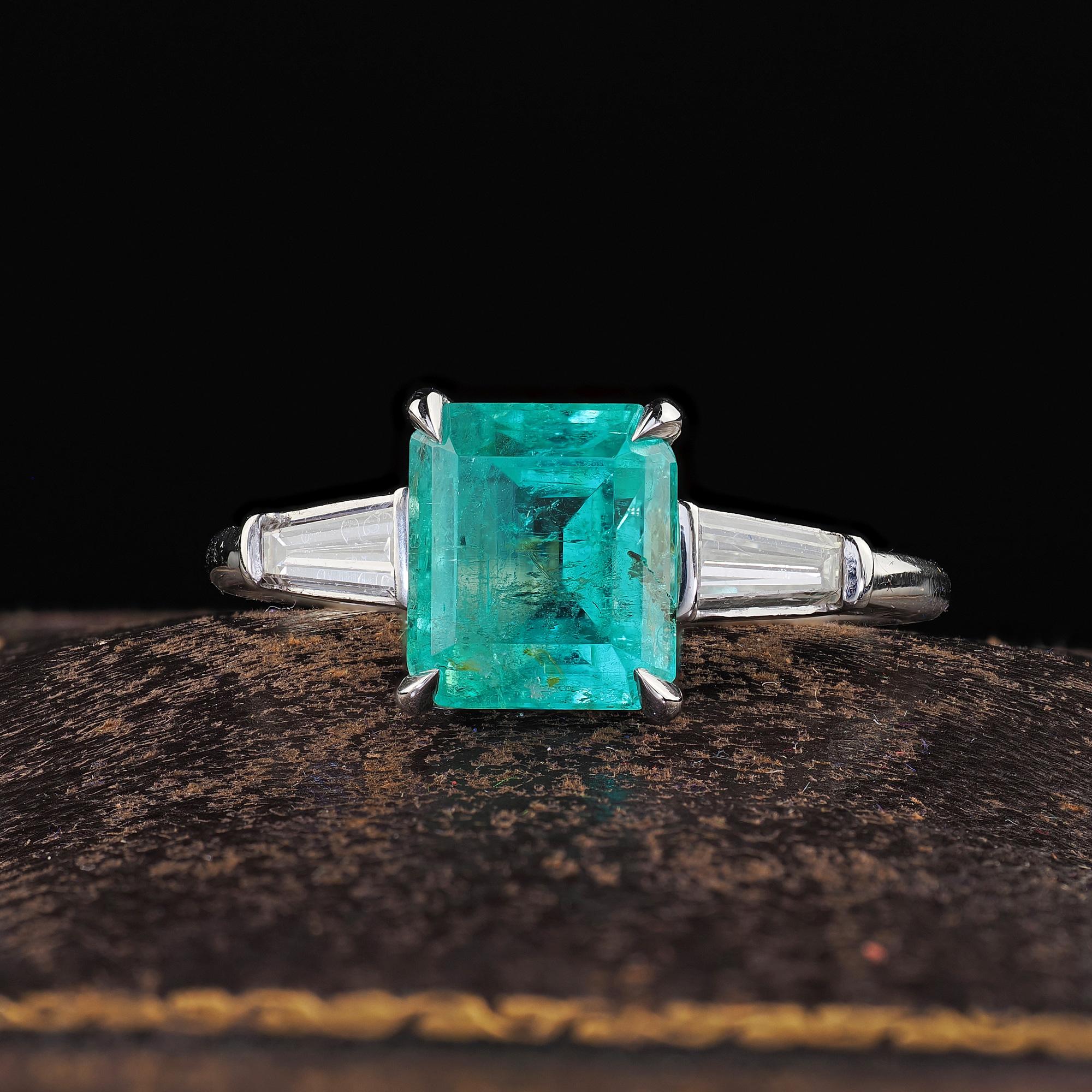Beautiful Antique Art Deco Platinum Emerald and Diamond Engagement Ring. This classic Art Deco emerald and diamond ring is crafted in platinum. This ring features a beautiful minty green Colombian emerald in the center with two tapered baguette