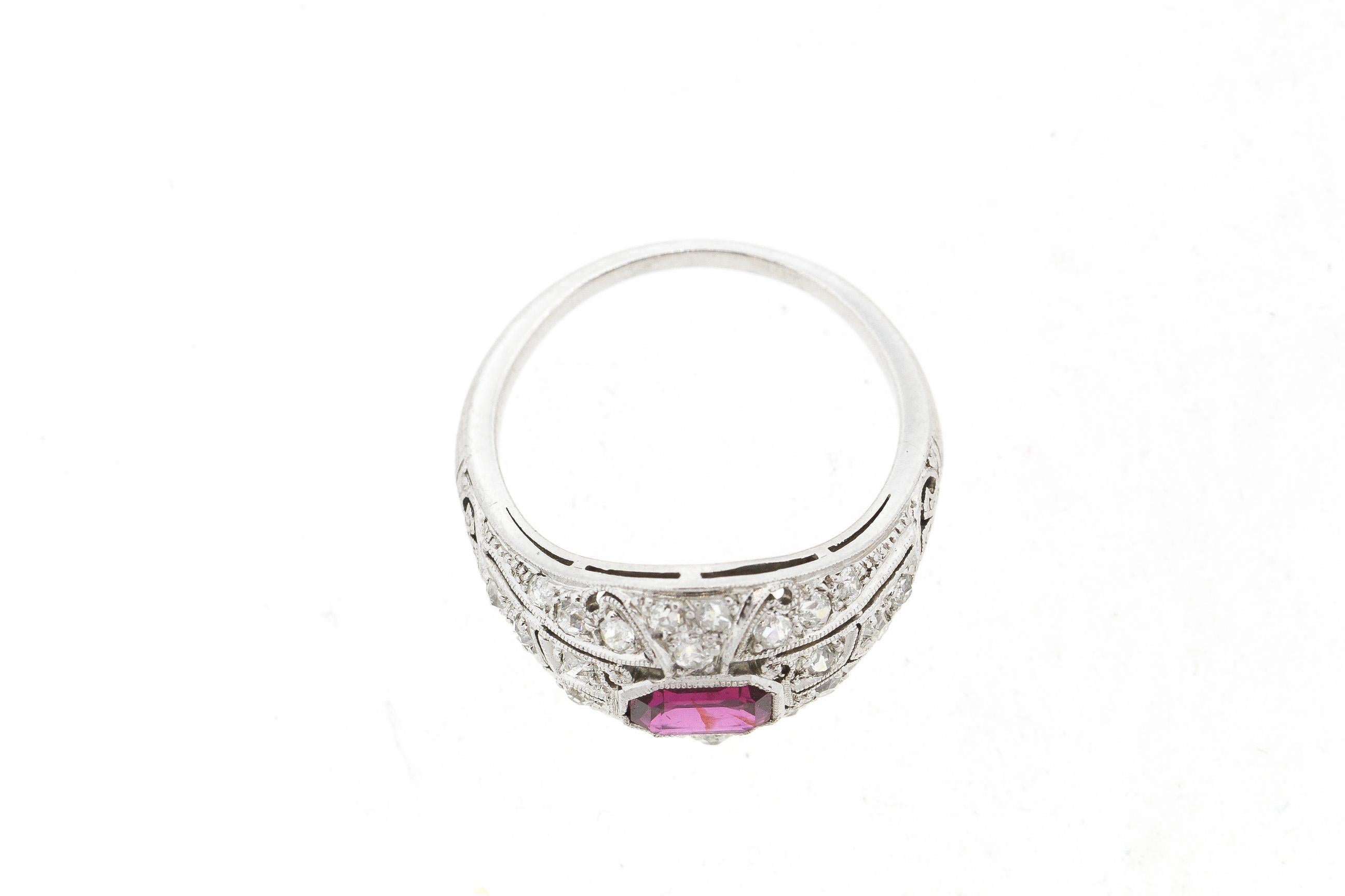 An antique Art Deco platinum diamond and rectangular shape ruby ring. The ruby is set in a beautiful original filigree platinum mounting set with numerous old single cut diamonds. Delicate scrolls and leaf pierce work adorn the mounting. The ruby is