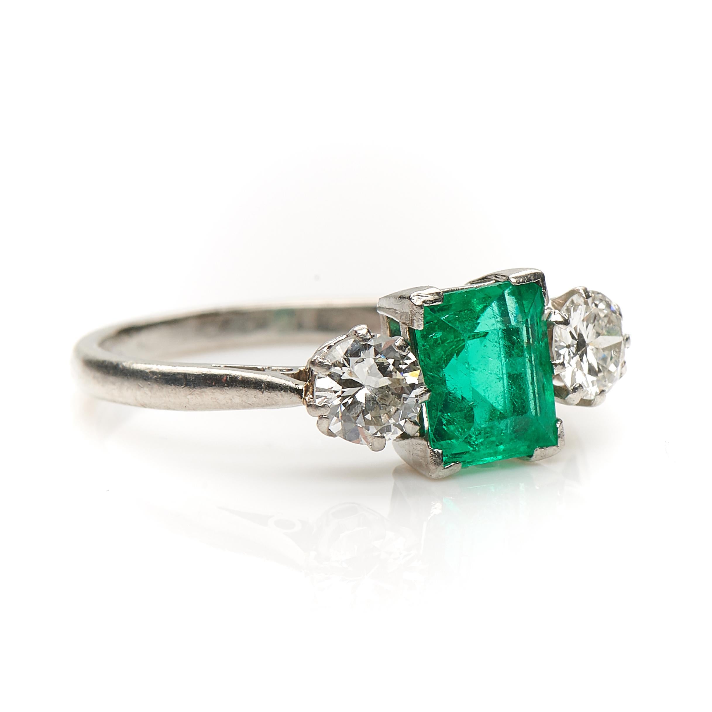 Art Deco, emerald and diamond ring, circa 1930. Centre set step-cut emerald flanked by two old-cut diamonds in a simple platinum setting. The emerald is a beautiful fresh green colour and the diamonds are bright white and have a lively sparkle,