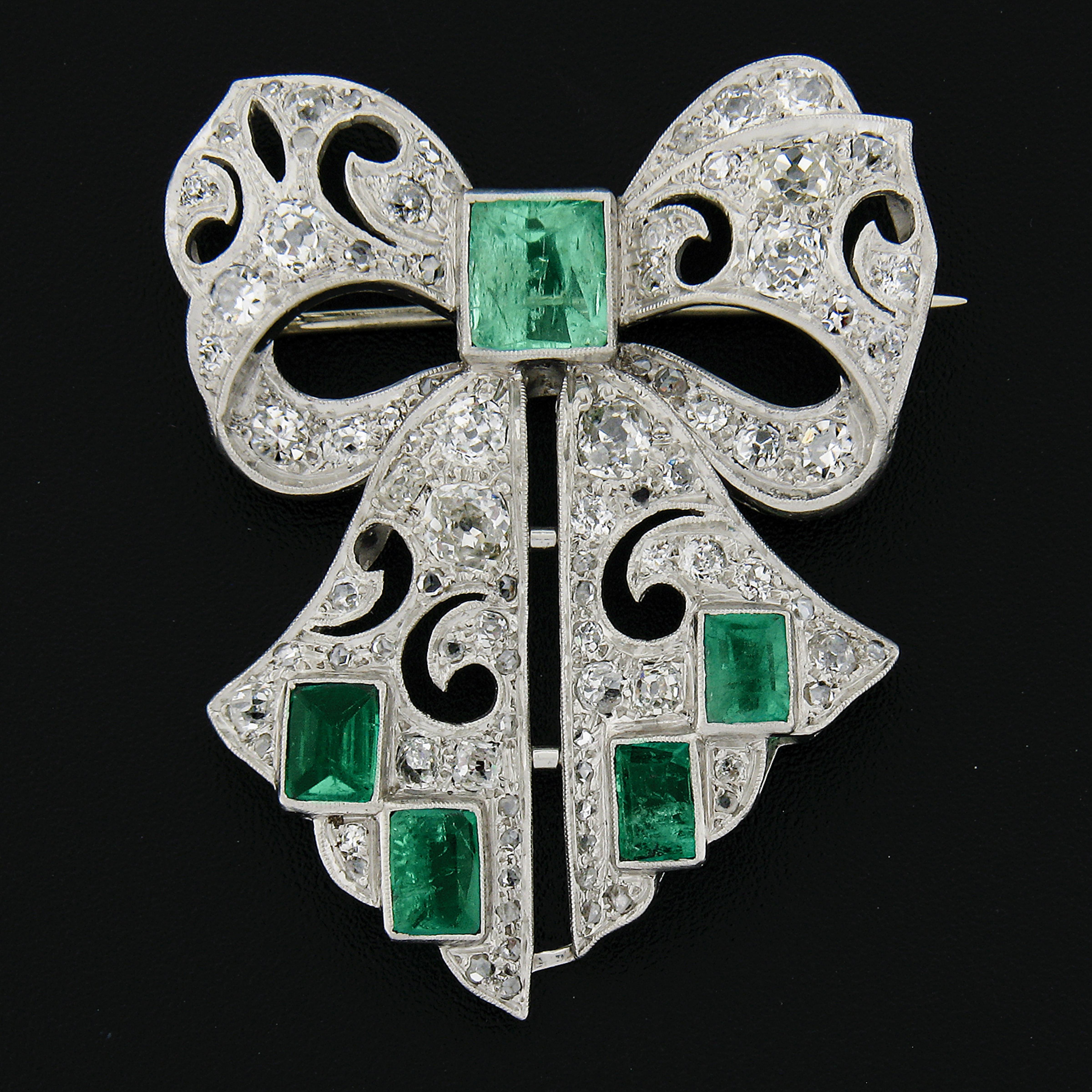 This magnificent antique bow pin brooch was crafted in solid platinum during the art deco period. It is adorned with with large and fine quality natural green emerald stones and drenched entirely with old cut diamonds. These emeralds add such a rich