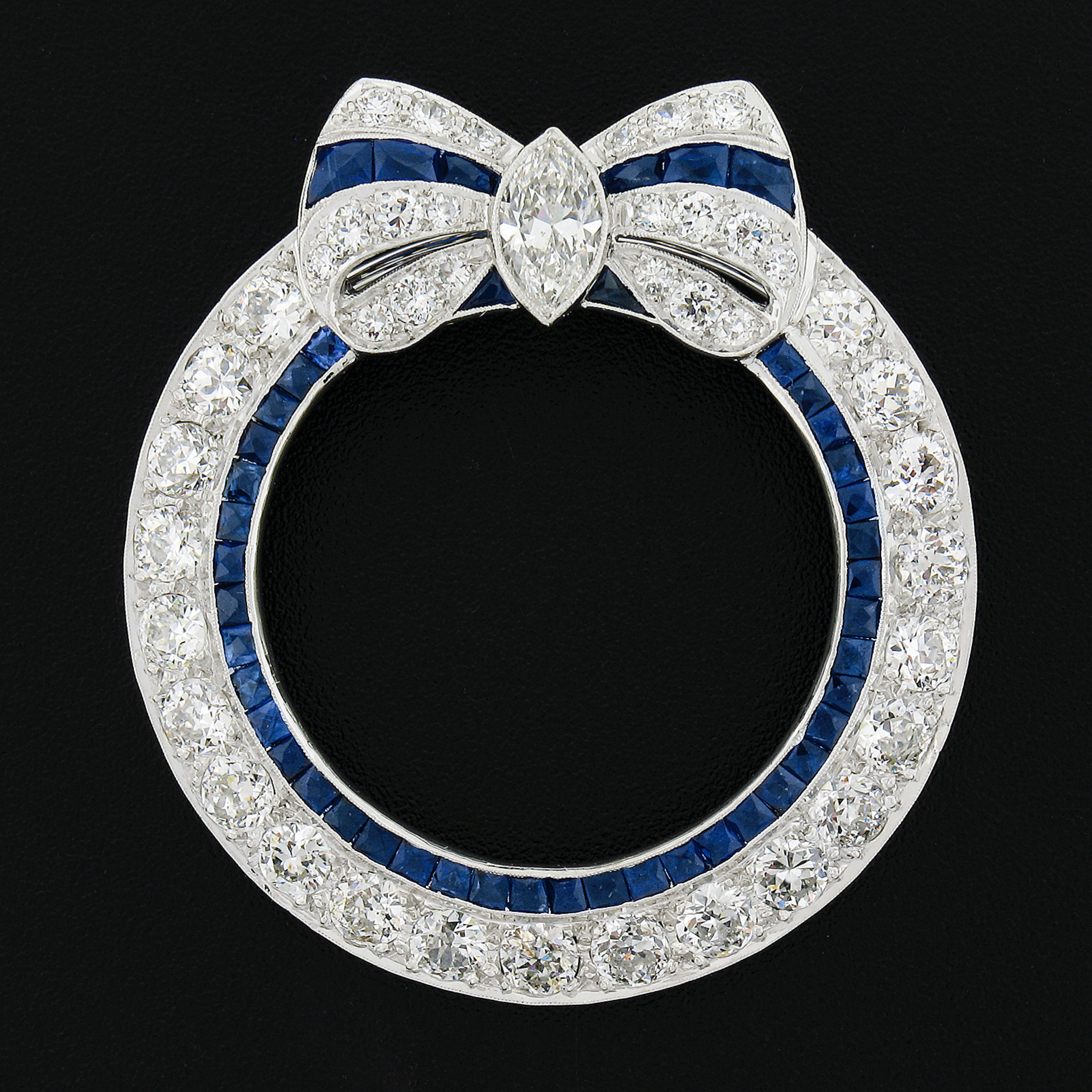 This breathtaking and large antique wreath brooch was crafted in solid platinum during the art deco period. The wreath is decorated with a beautiful bow design that is set with a large old marquise cut diamond at its center. The remailing of the bow