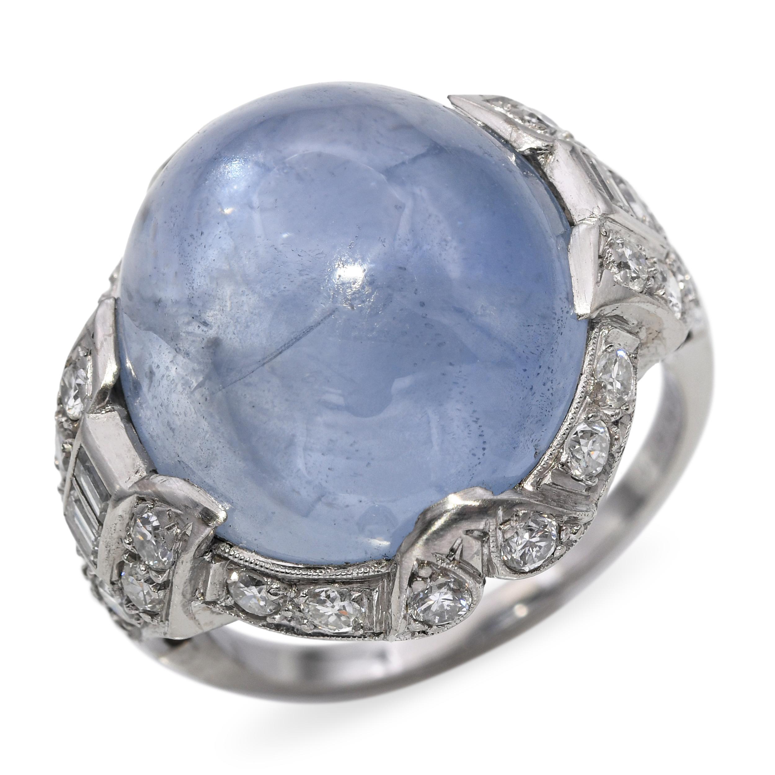 Cette bague de cocktail Art déco spectaculaire est centrée sur un saphir étoilé cabochon captivant, son corps soyeux montrant le jeu de lumière enchanteur qui donne à la gemme son nom céleste. D'un poids considérable et de forme bombée, le saphir