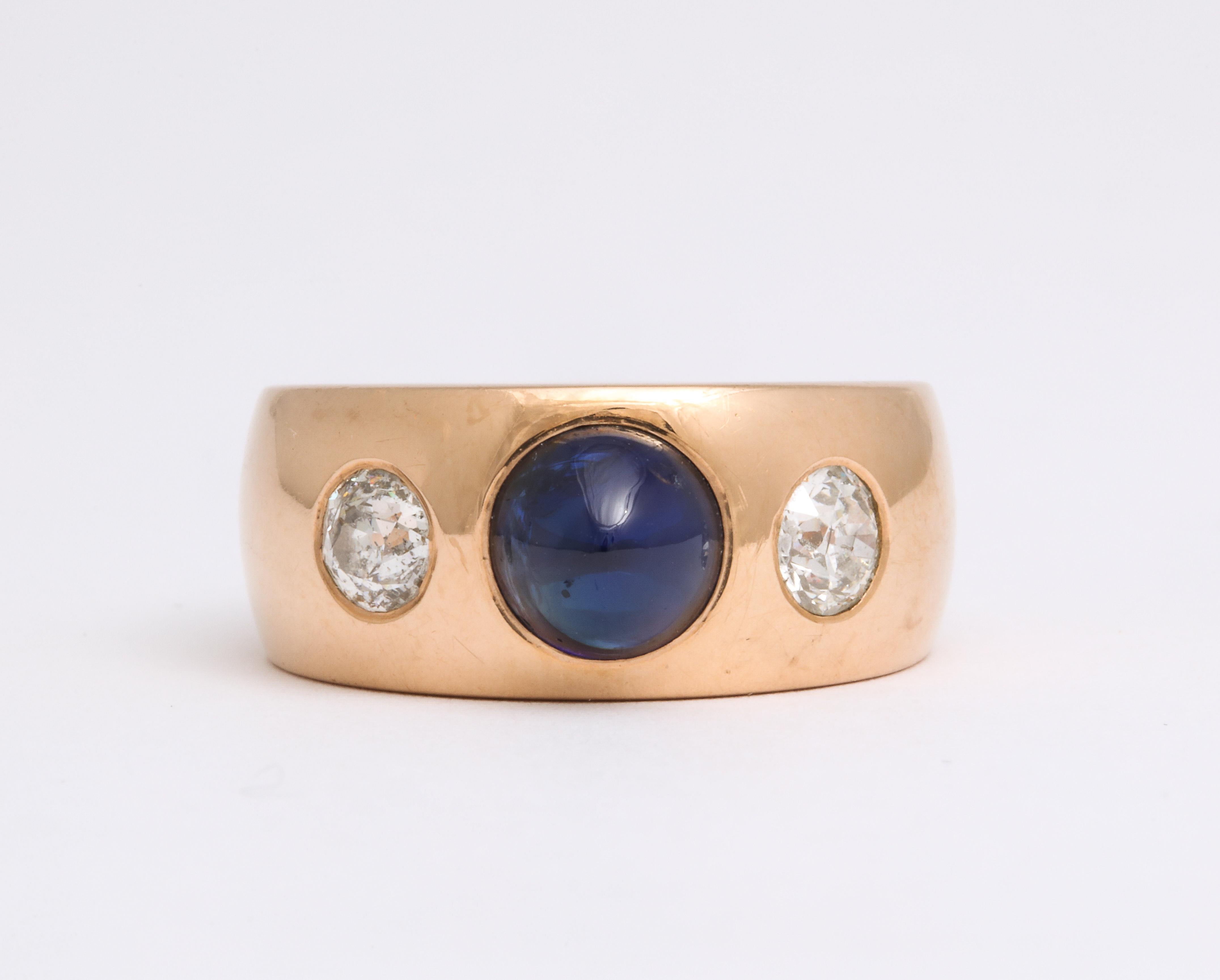 Solidly Art Deco in design, solid in weight, this stunning 18 Kt gold band is set with a sugarloaf natural sapphire, (a cabochon cut gem that rises to a dome), weighing 1.6 Cts and two European cut diamonds totaling approximately 1 Ct in weight. The