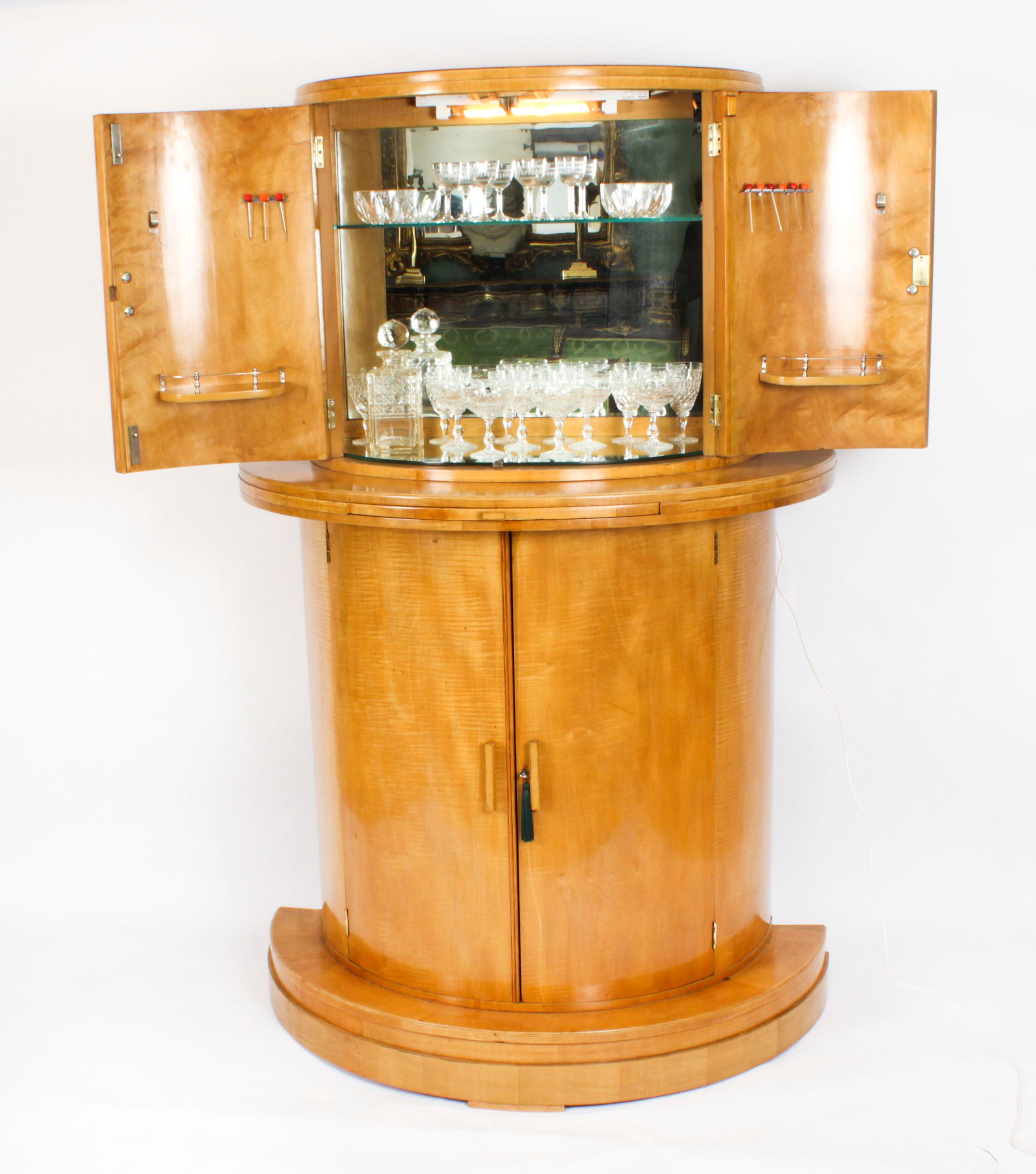 This is a fantastic antique Art Deco satinwood demi lune cocktail cabinet by Hille and suit of Cut Crystal Glasses circa 1920 in date.
 
It is of architectural form, made in figured satinwood, the upper part comprises a pair of doors enclosing a