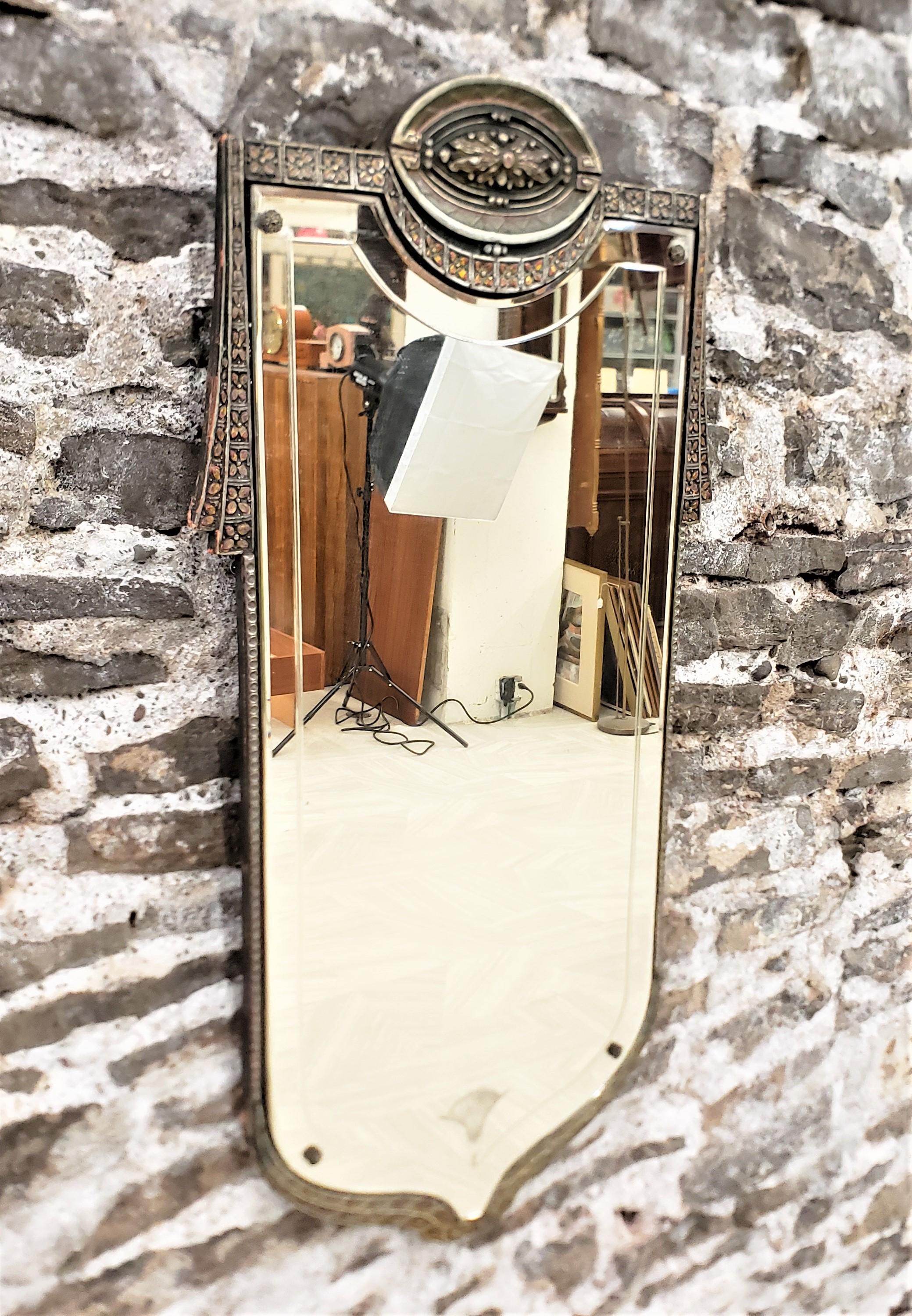 This antique wall mirror was made in the United States by an unknown maker, and dates to approximately 1920 and done in a period Art Deco style. The mirror is shield shaped with a beveled edge and an etched border and stylized fan at the bottom. The