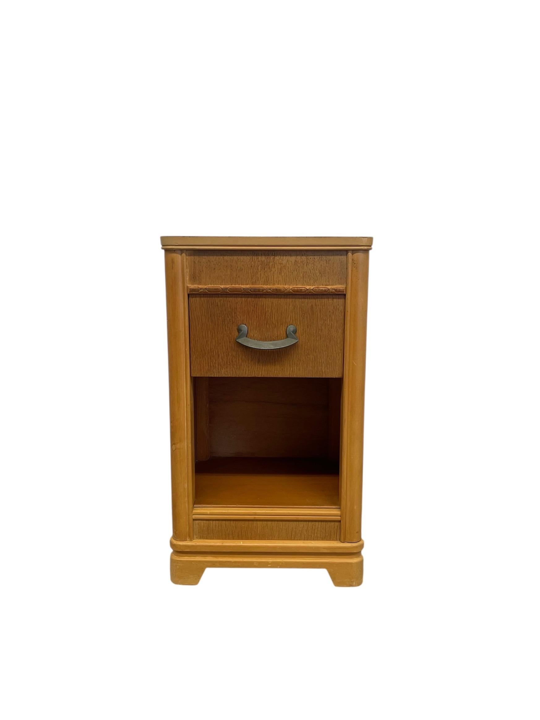 Questo tavolino antico in stile Art Déco presenta un design compatto e funzionale con dettagli classici d'epoca. Realizzato in legno massiccio con una calda finitura color miele, il mobile comprende un cassetto superiore con l'originale maniglia in