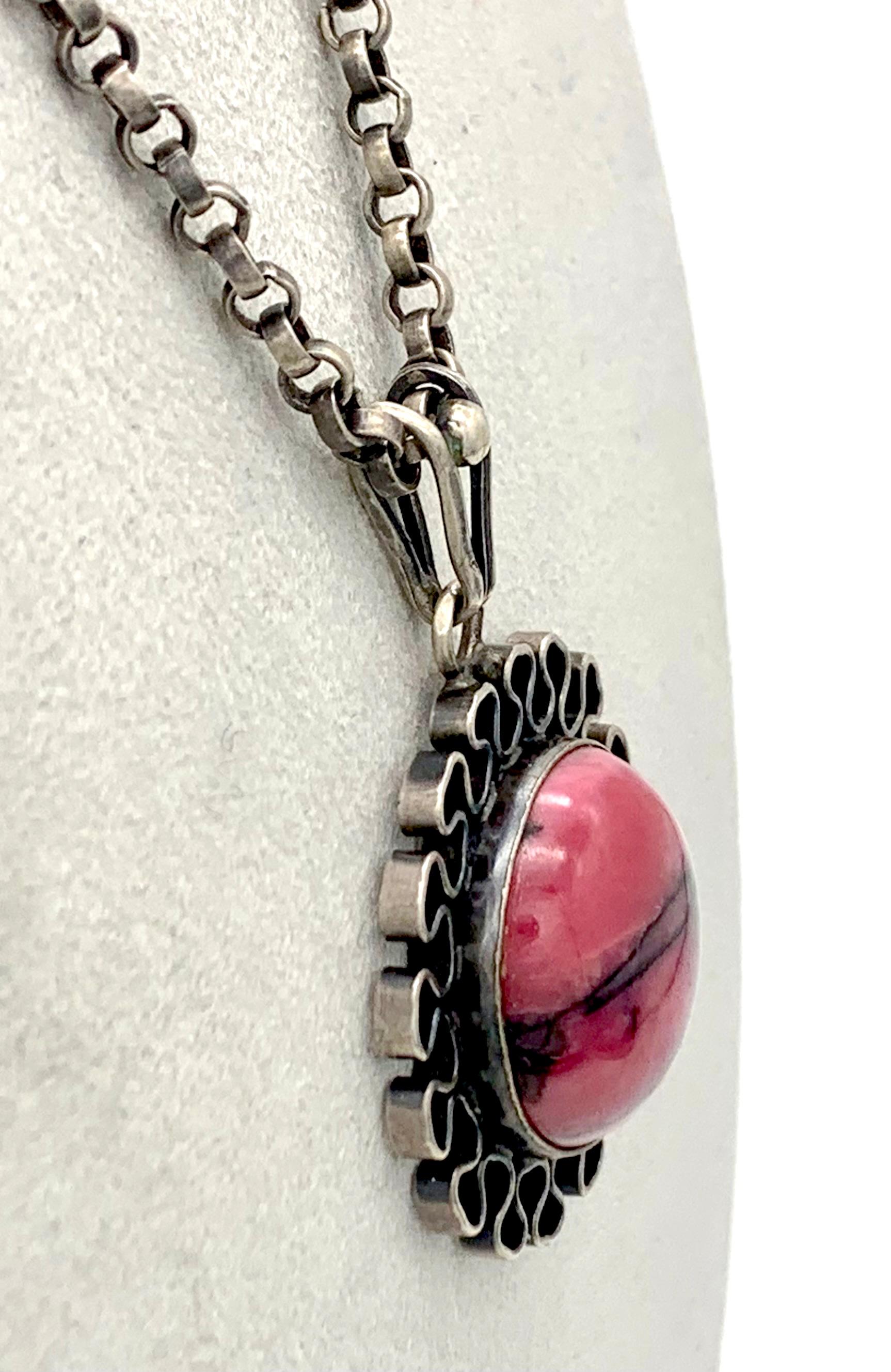 Ce pendentif moderniste en argent Art déco a été fabriqué à la main au début des années 1920. Il est conçu comme une fleur stylisée. Le centre du pendentif est serti d'un cabochon de pierre dure rose intense avec des inclusions noires expressives. 