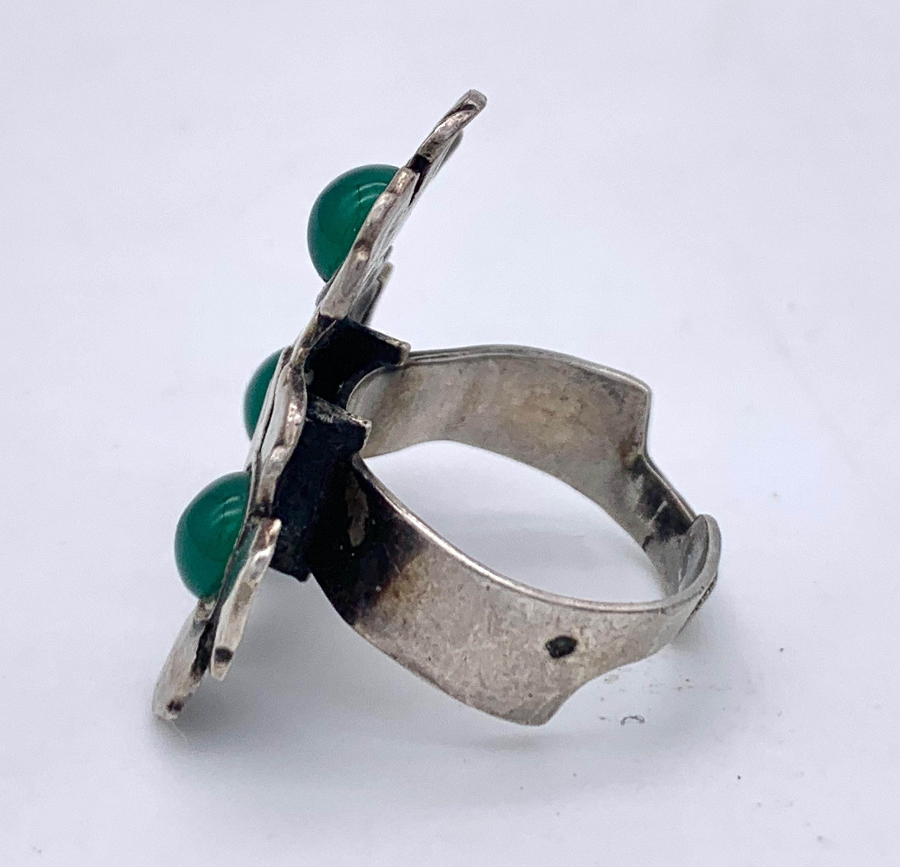 This charming ring was made out of silver in 1920 ca. It is designed as a cluster of three flowers, each flower is set with a green chalcedony cabochon. The ring is impressed with the French crab silver hallmark. The ring is signed with a French