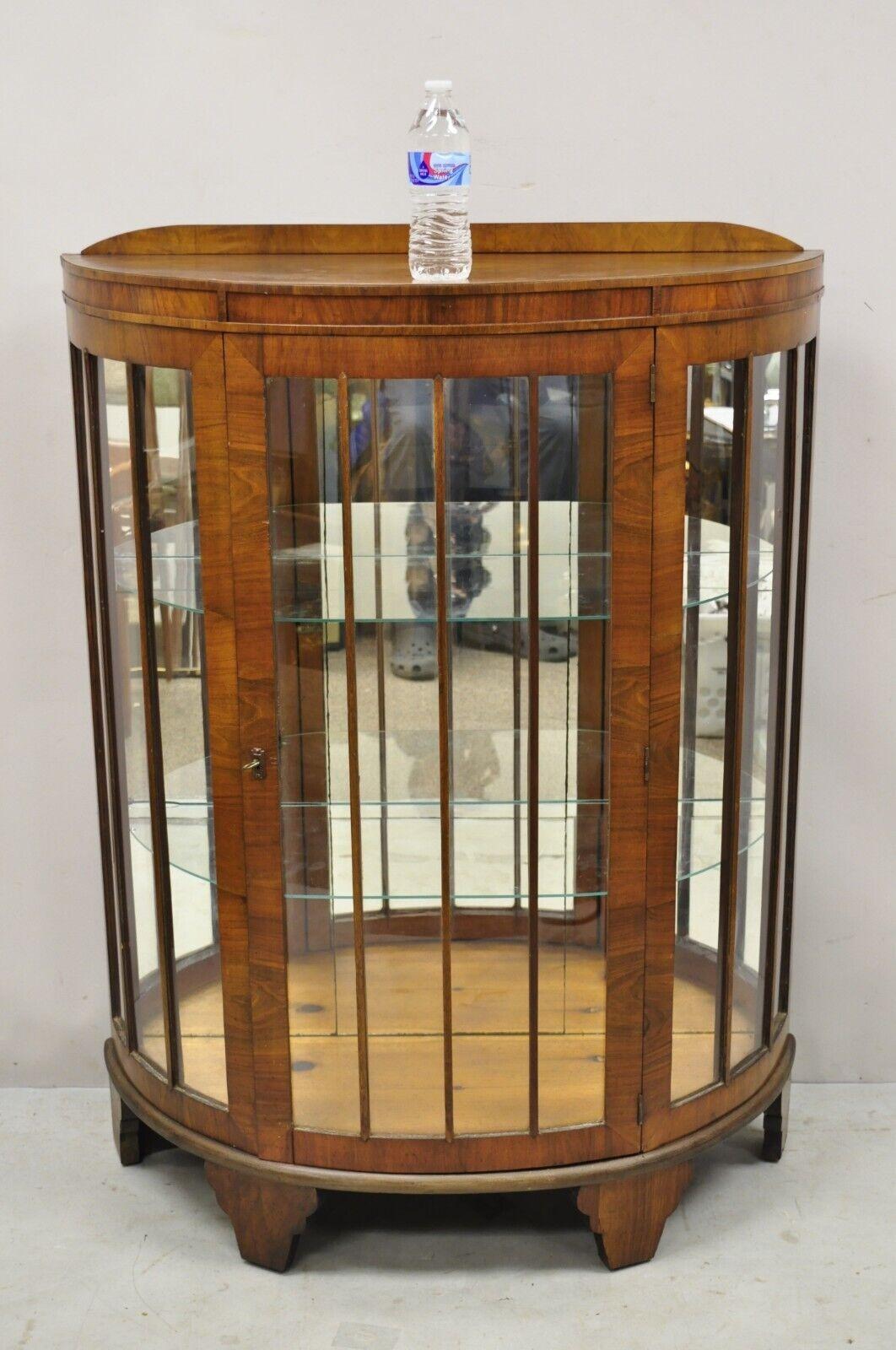 Antique Art Deco small half round demilune walnut Curio display cabinet. Item features mirrored backing, half round demilune form, beautiful wood grain, 1 swing door, working lock and key, very nice antique item. Circa Early 1900s. Measurements: 48