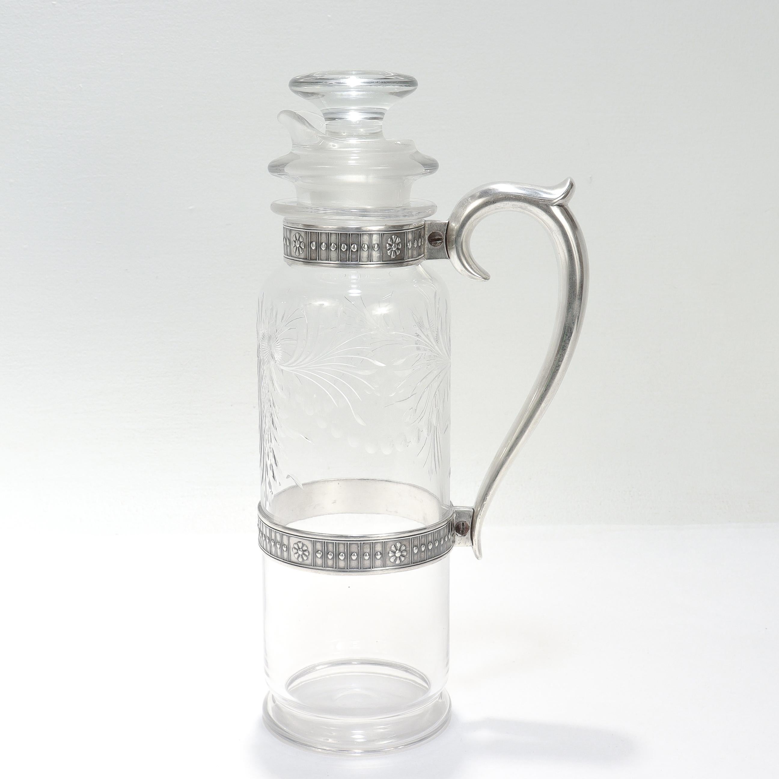 Una fina jarra americana del periodo Art Déco.

En cristal tallado.

Con asa de plata de ley y bandas de plata alrededor del cuerpo y el cuello. 

Decorada con motivos de flores y hojas recortadas. 

Con colador/pitorro extraíble y tapa.

Marcado en