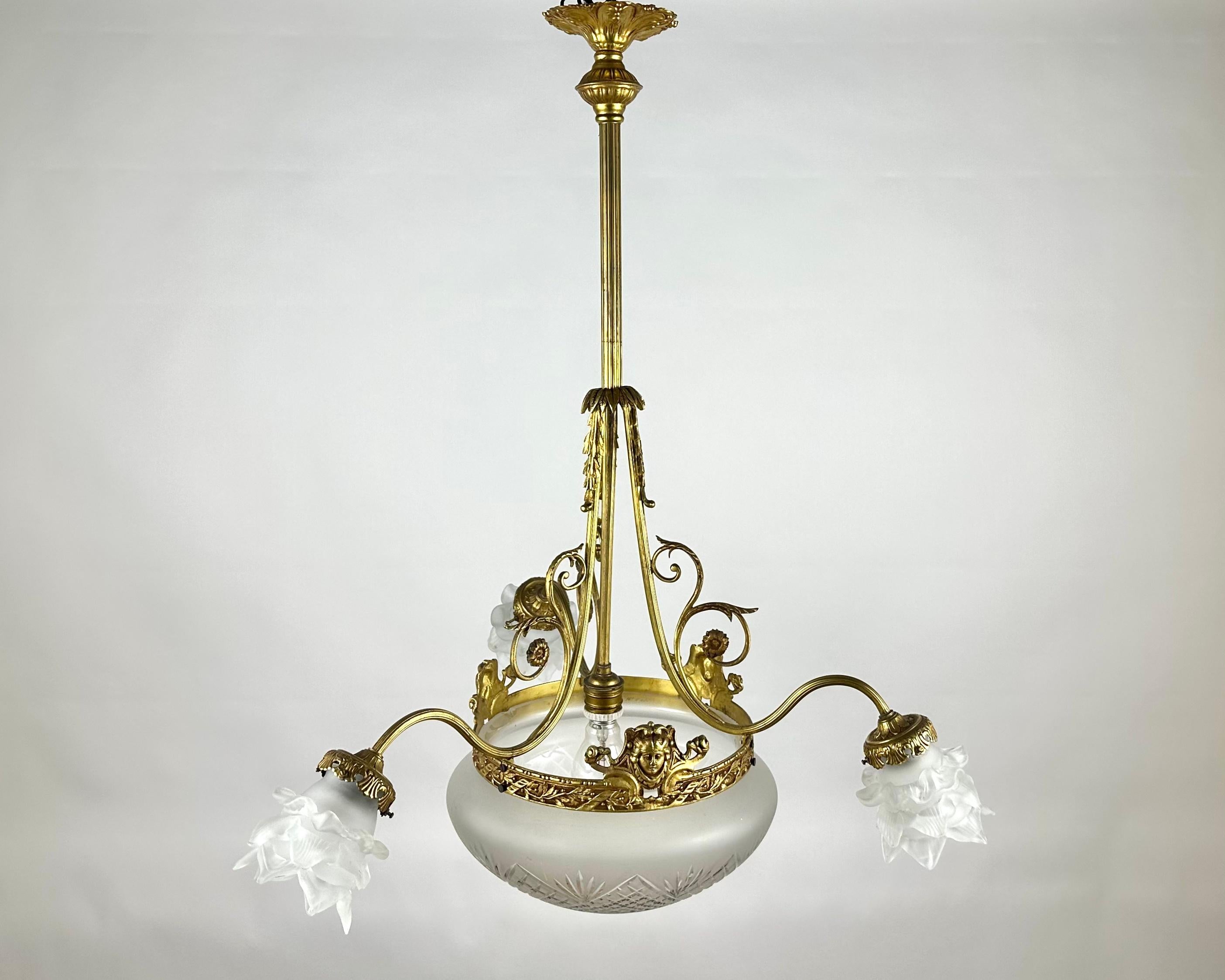 Beautiful Antique Chandelier is manufactured in France, in 1920s. 

Three white matte lampshades framed by aged bronze look, on the one hand, laconic, on the other - elegant.

In the center there is a round closed lampshade, which ensures an even