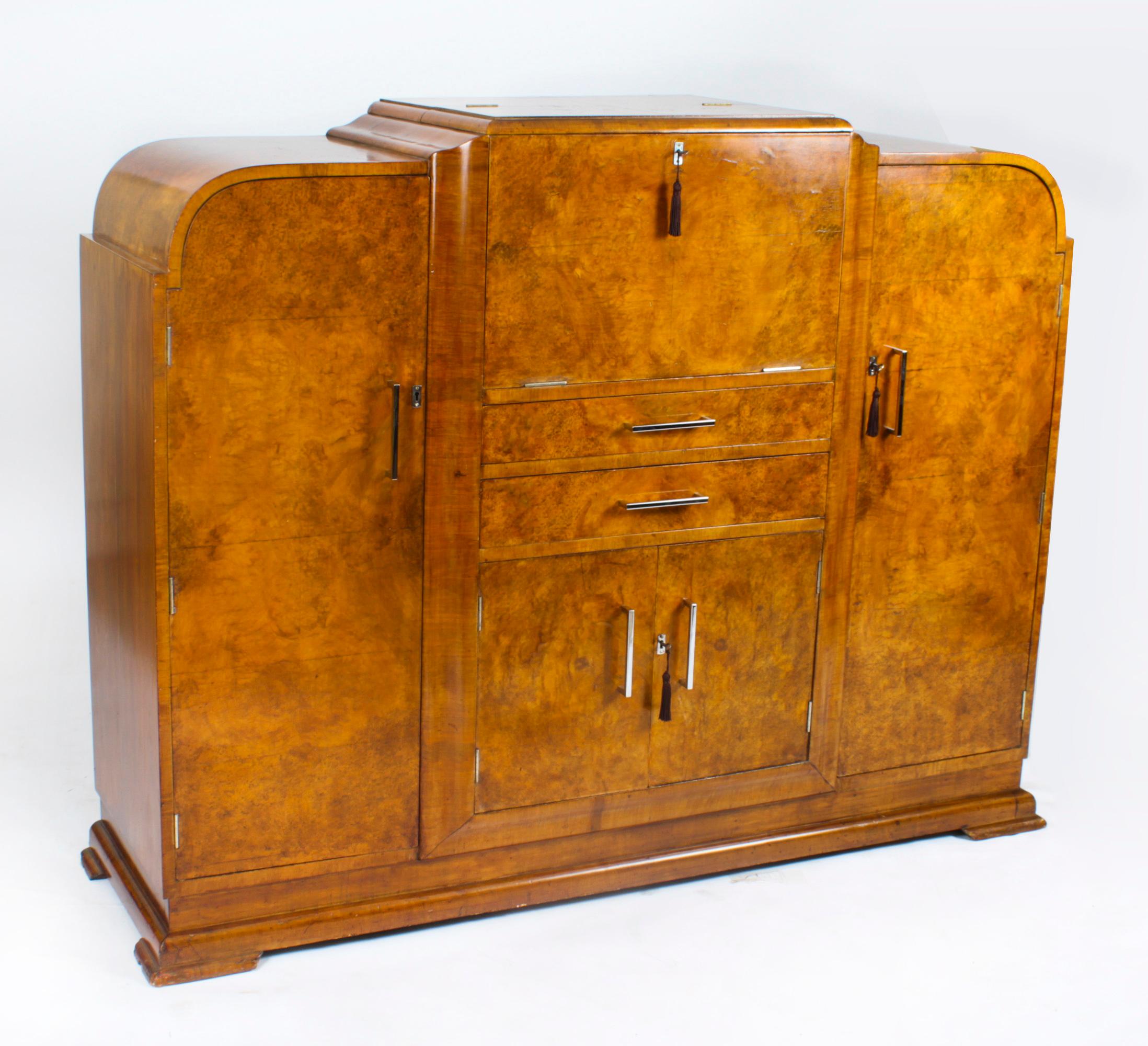 This is a superb antique Art Deco burr walnut cocktail cabinet sideboard complete with glassware, circa 1920 in date.
 
The upper part comprises a fall front that opens to reveal a striking fitted mirrored interior and comes complete with a suite