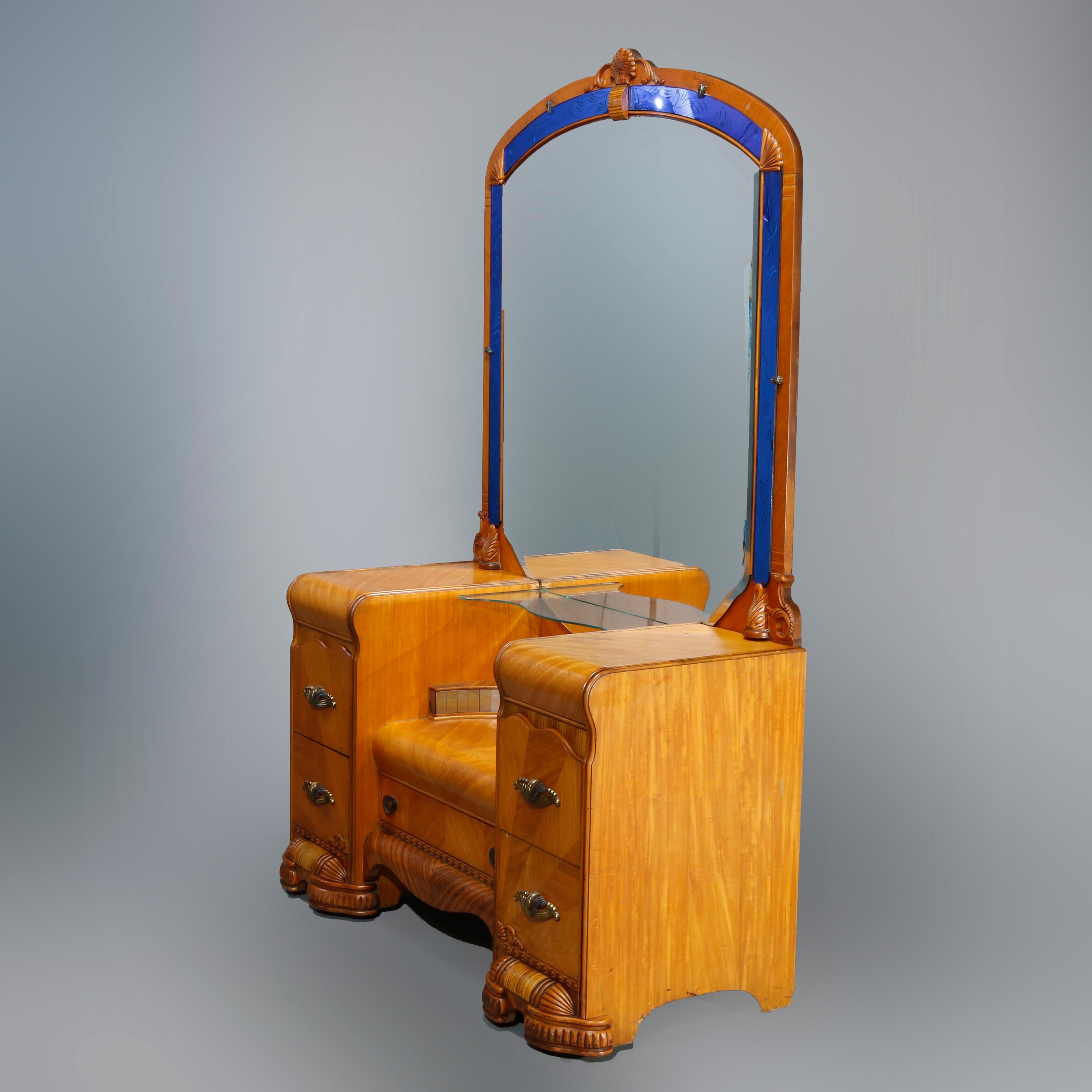 An antique Art Deco waterfall vanity set offers mahogany construction with shaped mirror having shell carved crest and foliate etched blue glass bordering surmounting sunken chest with satinwood inlay across drawers and stylized foliate cast pulls